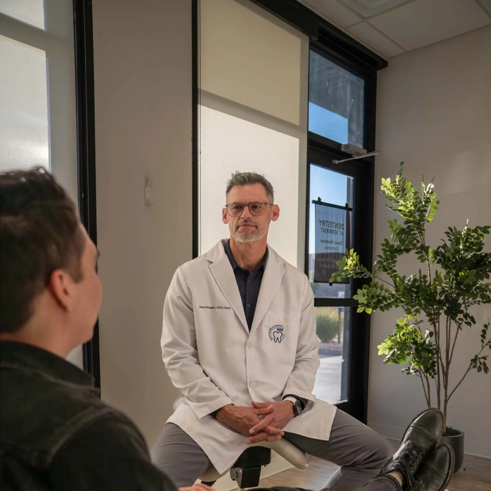 Young blonde girl in rainbow sweater crouching on carpet with paper crafts in hand indoors.