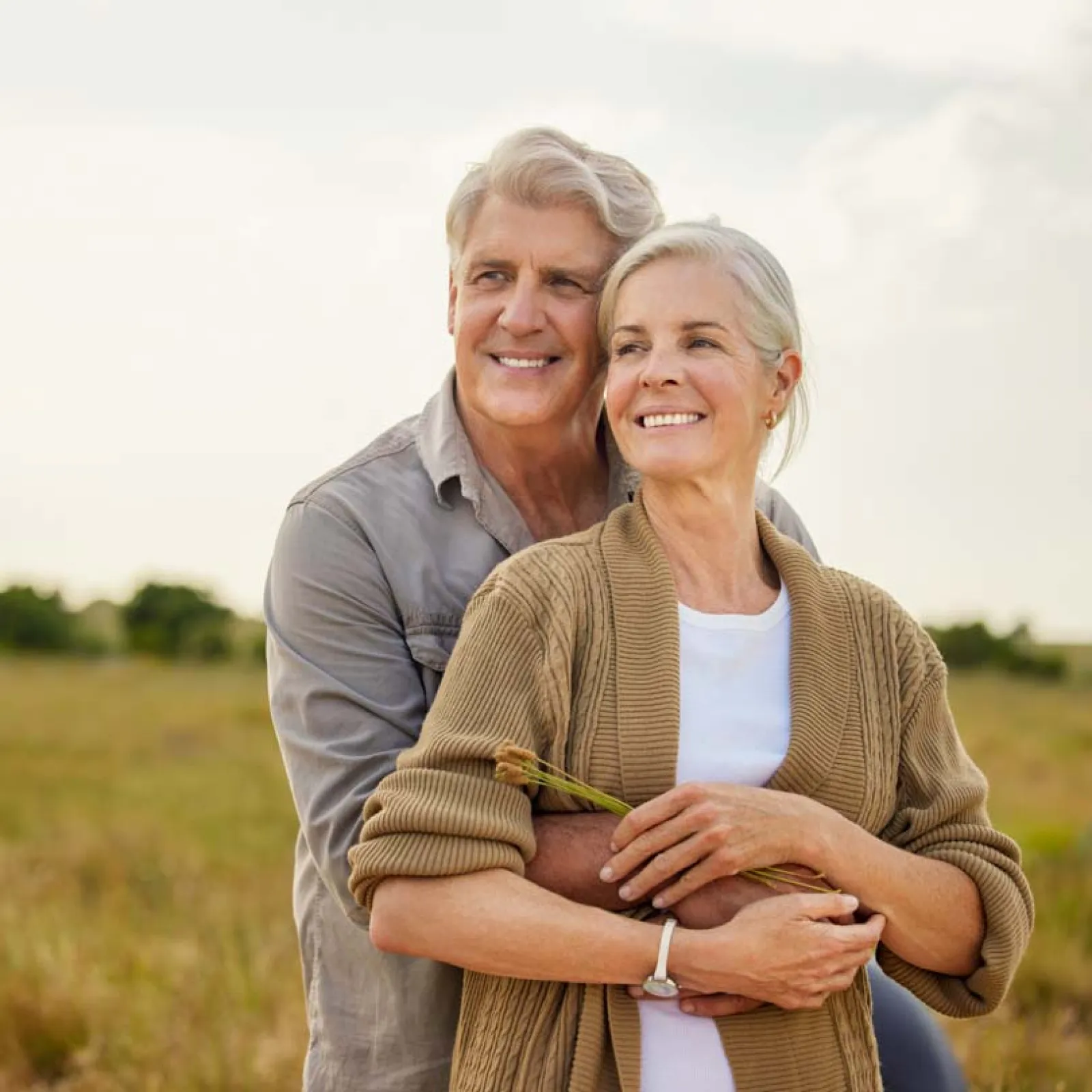 Smiling senior couple embracing outdoors in a field during a sunny day, enjoying peaceful nature together.