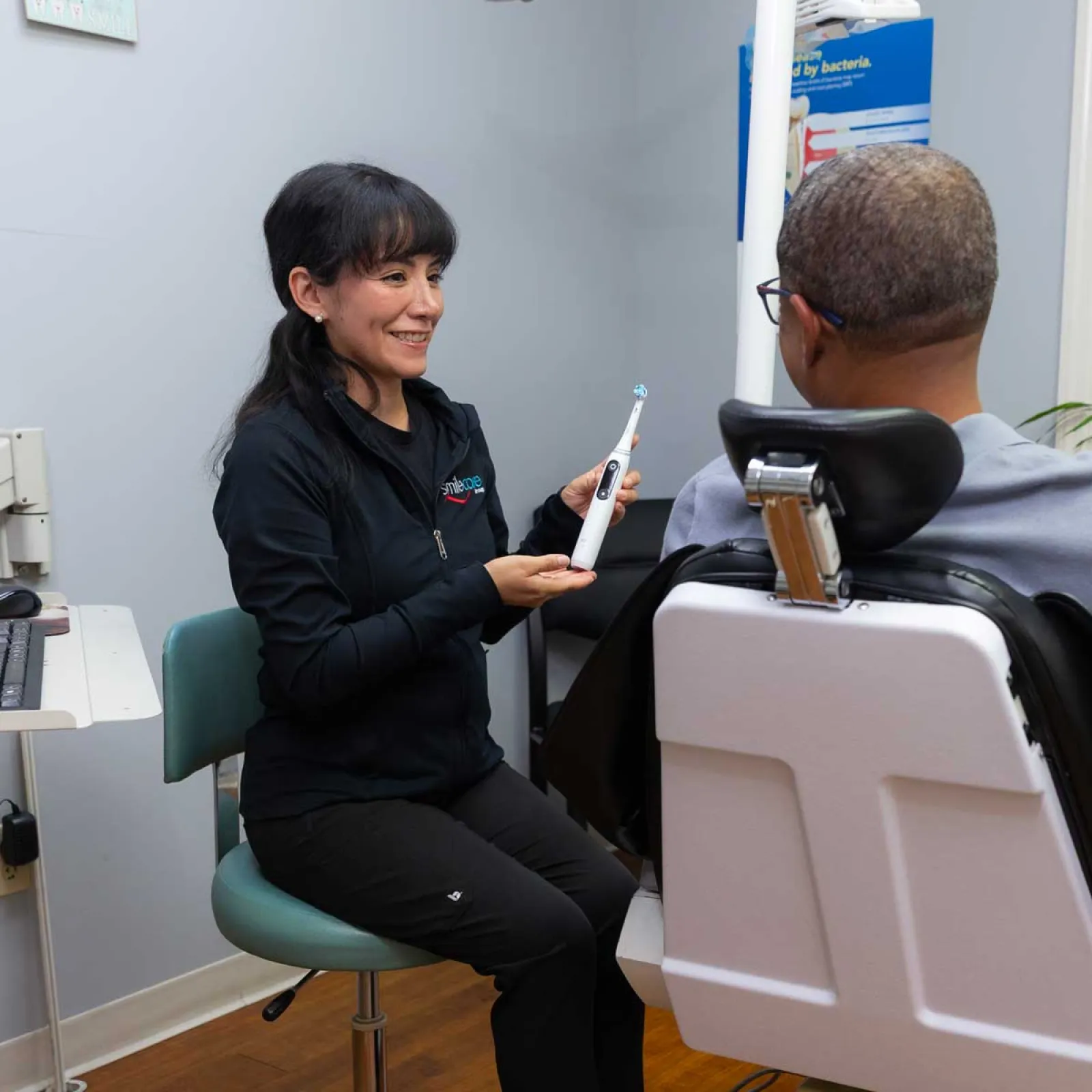 Dentist explaining electric toothbrush use to patient in bright dental office near window.
