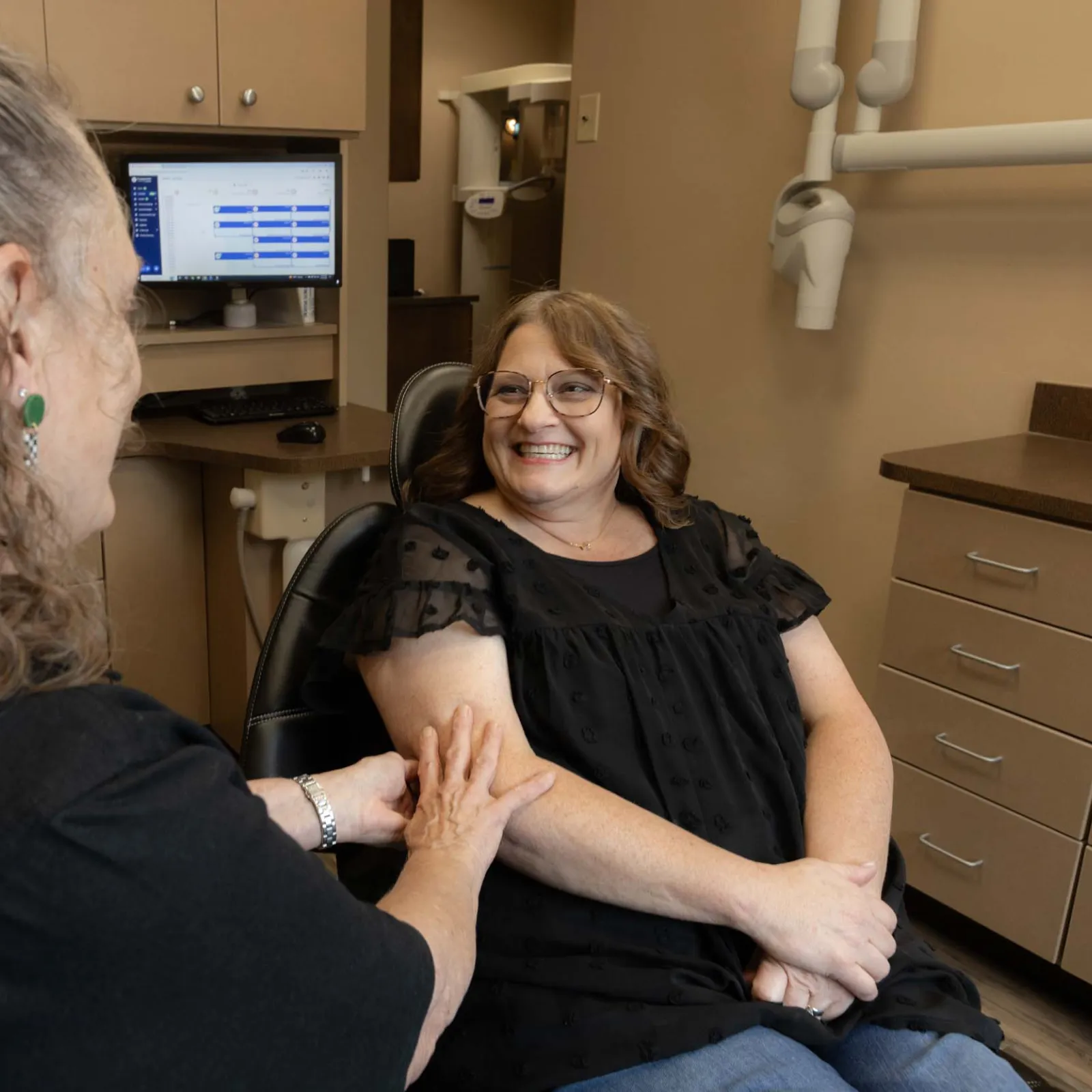 Woman smiling while sitting in a dental chair, consulting with a female dentist in a dental office.