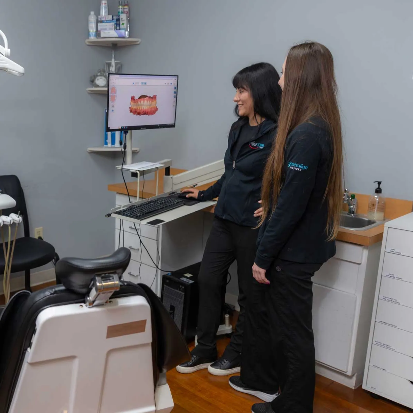 Two dental professionals review a 3D dental scan on a computer in a modern dental clinic room.