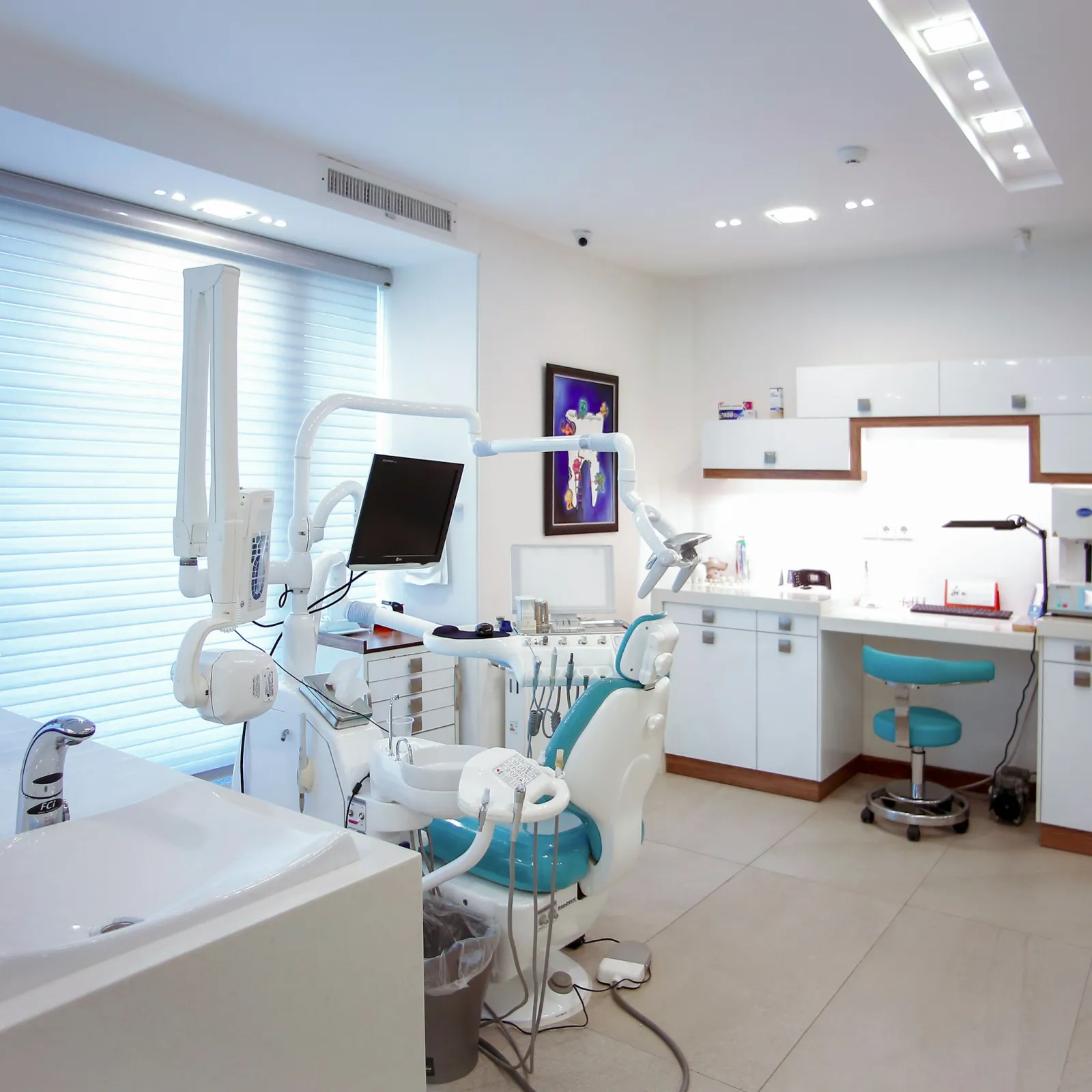 Bright modern dental clinic with dental chair, monitor, sink, and white cabinetry under natural light.