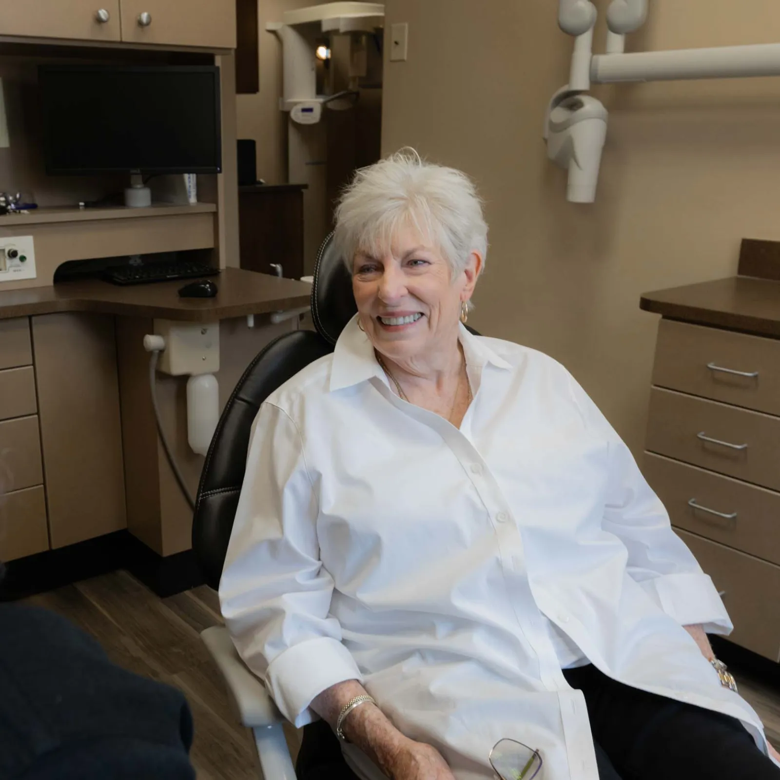 Senior woman smiling in dental chair during consultation with dentist in modern clinic room
