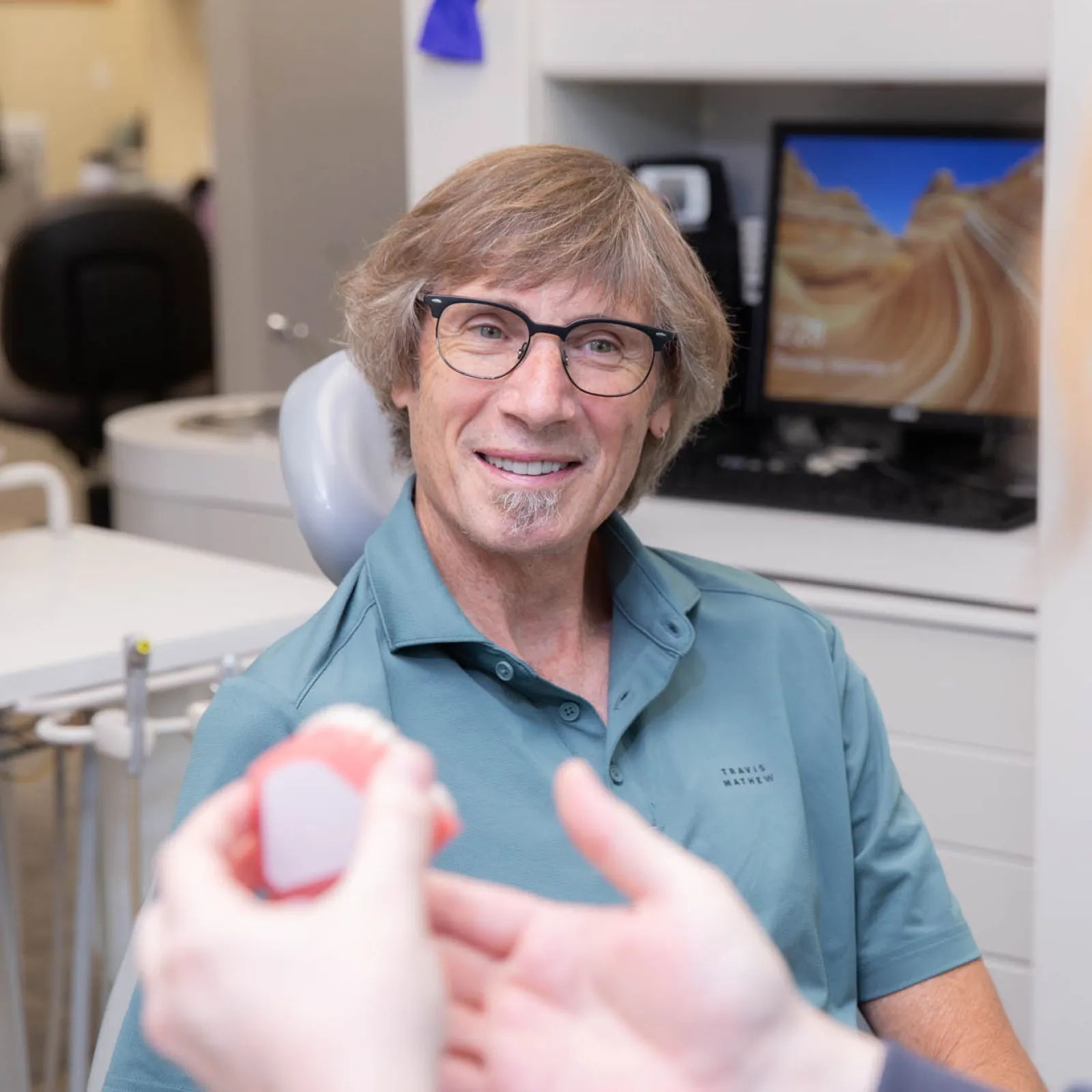 Smiling male dentist explaining a dental model to a patient in a modern dental office.