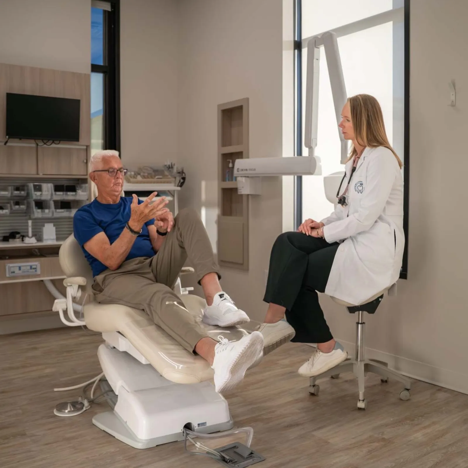 Doctor in white coat consulting an elderly male patient seated on a medical examination chair in a modern clinic.