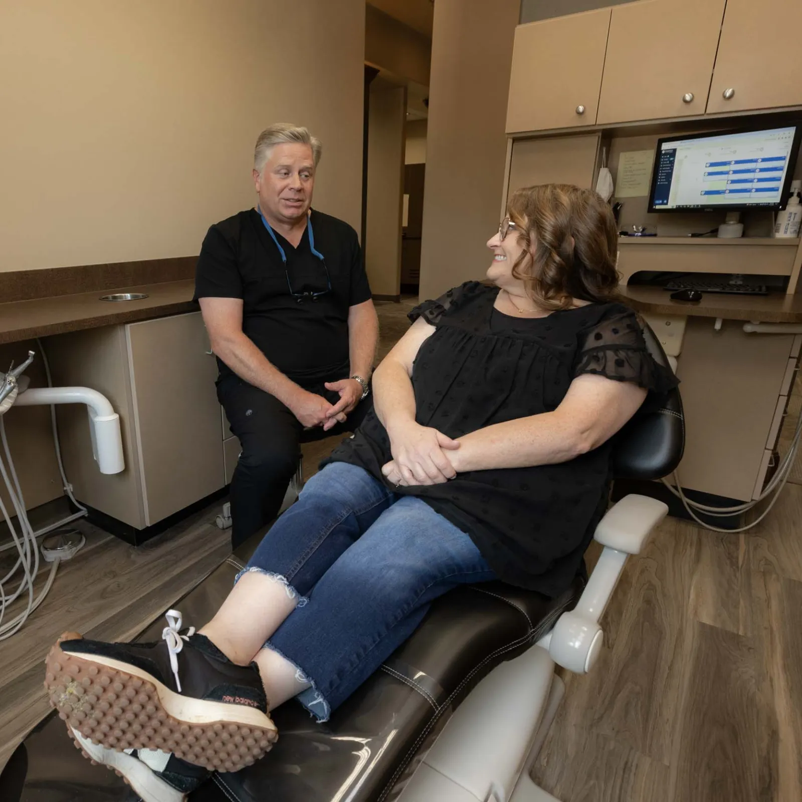 Dentist consulting with female patient seated in dental chair in a modern clinic room.