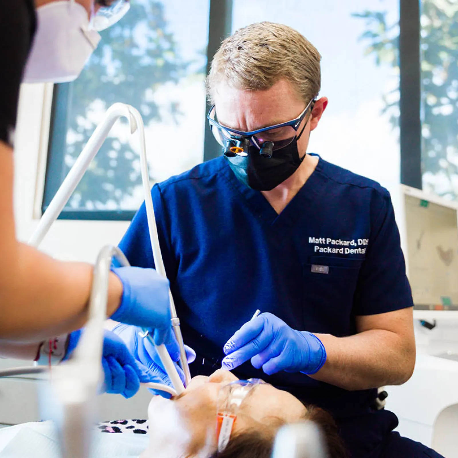 Dentist wearing magnifying glasses and gloves performing a dental procedure on a patient in a clinic.