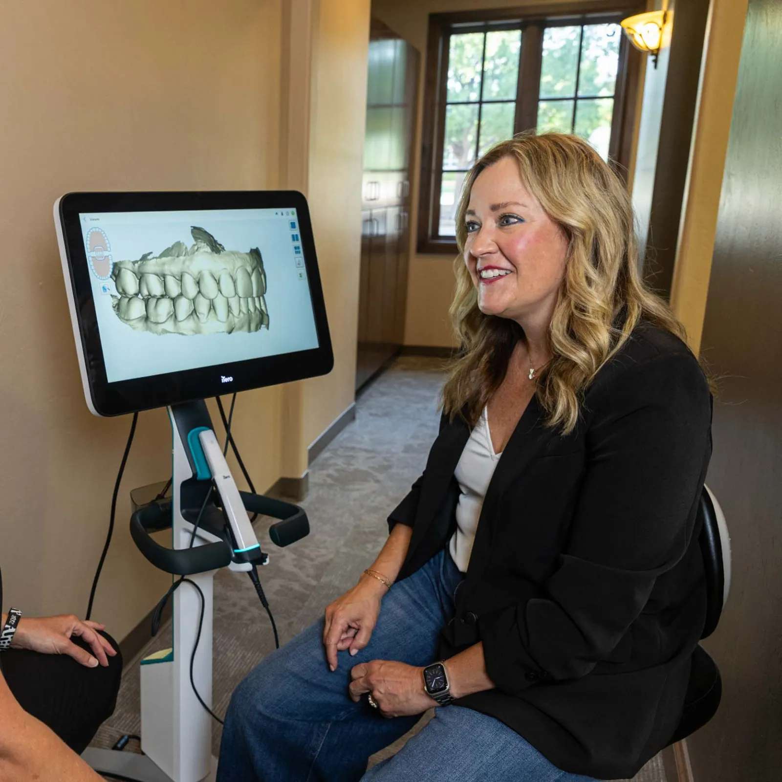 Dentist and patient discussing 3D dental scan of teeth on a screen in a clinic room.