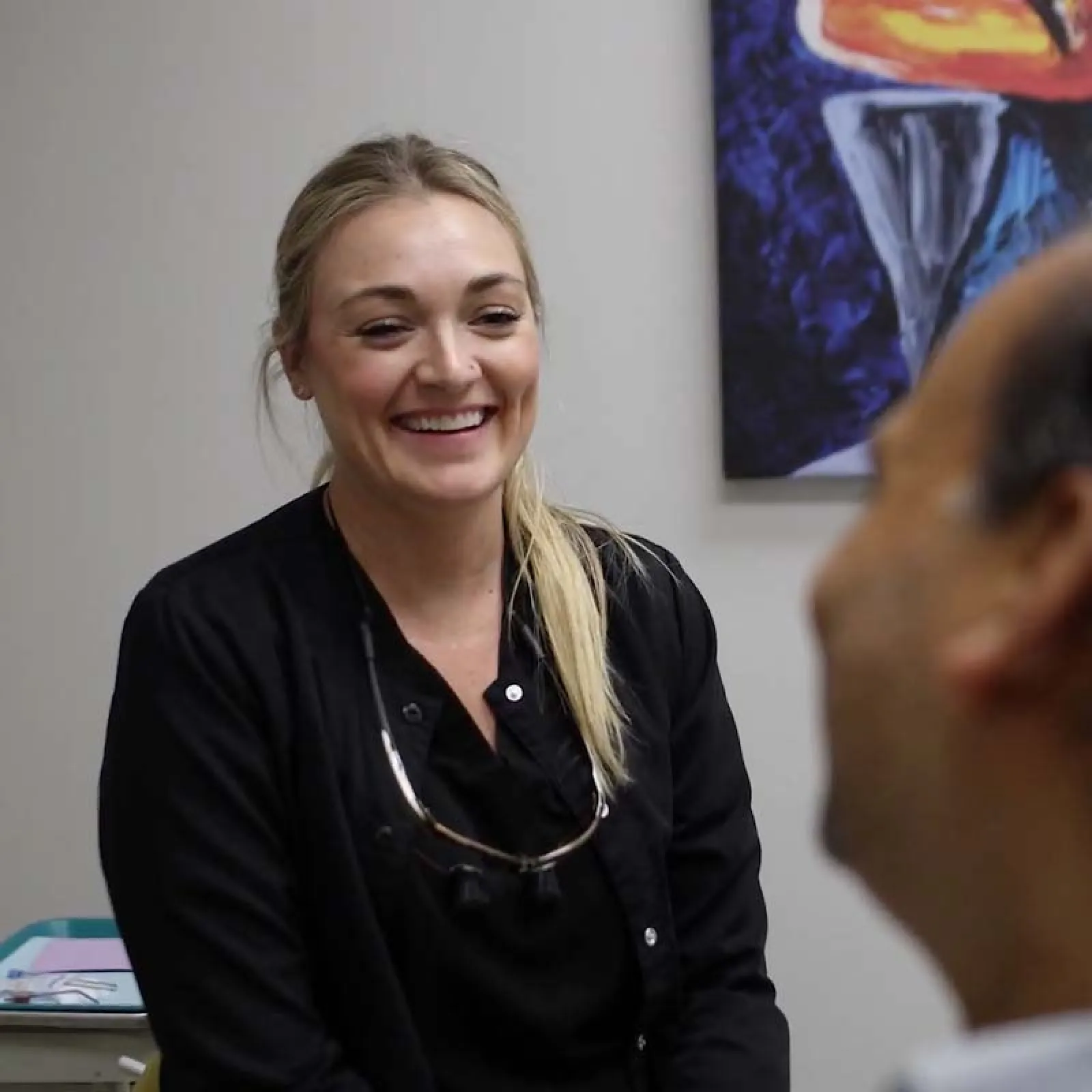 Smiling female dentist in black uniform talking with a patient in a bright dental office.