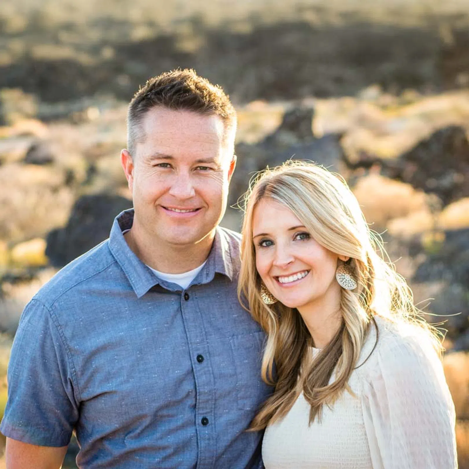 Smiling couple standing outdoors with a blurred natural rocky landscape in the warm sunlight background