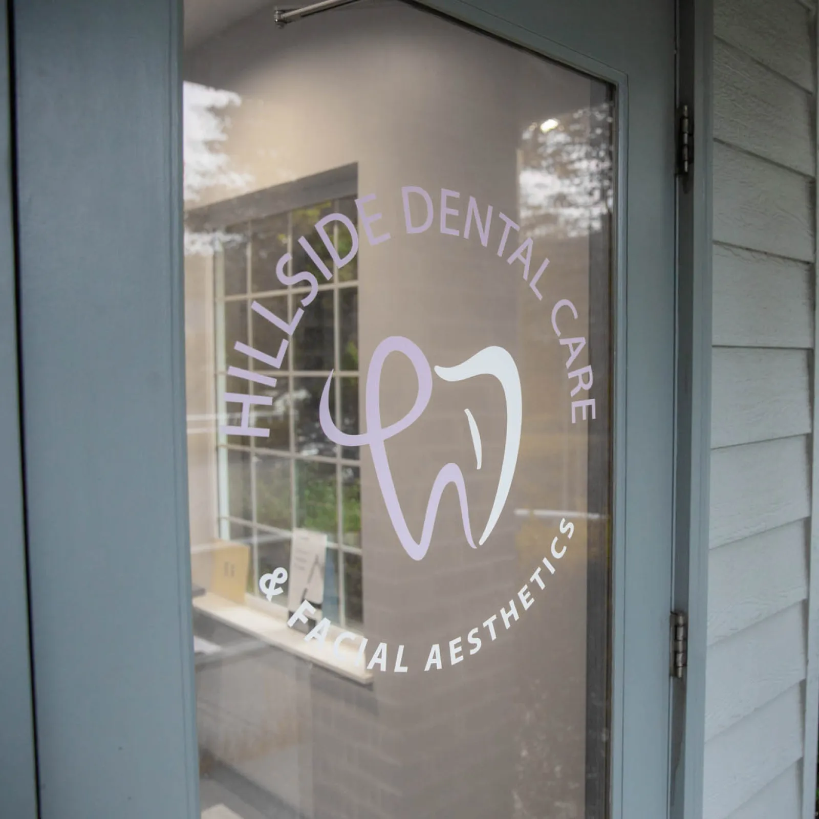 Glass door with Hillside Dental Care & Facial Aesthetics logo showing a stylized tooth design.