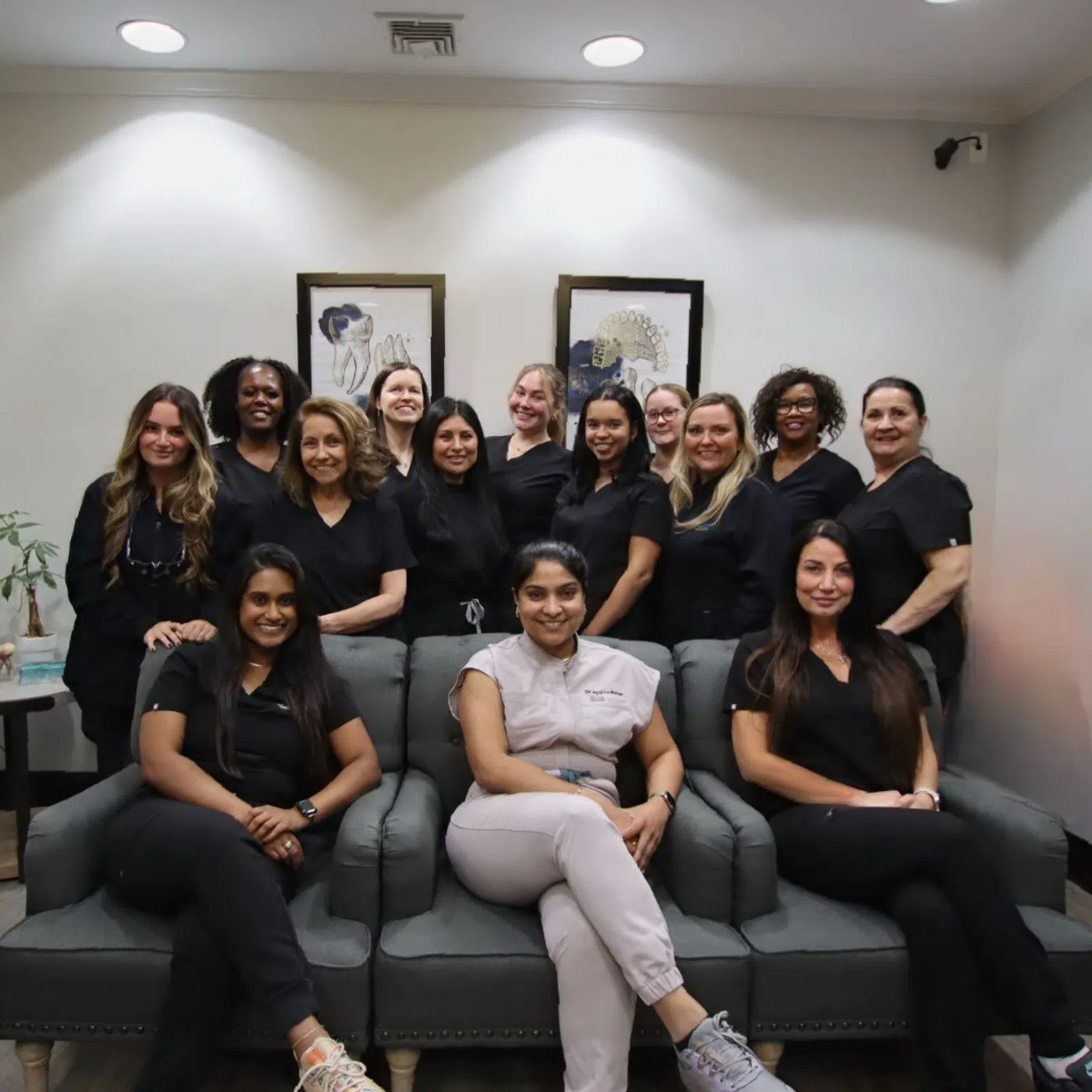 Group of diverse women in black and white uniforms posing together on sofas in a professional setting.