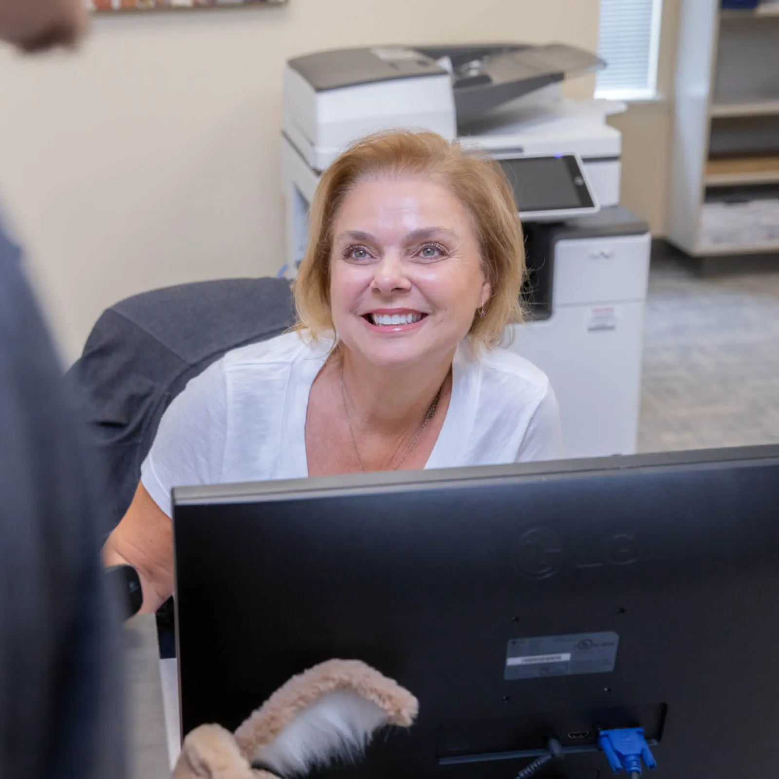 Smiling woman receptionist helping a visitor at the front desk in an office environment.