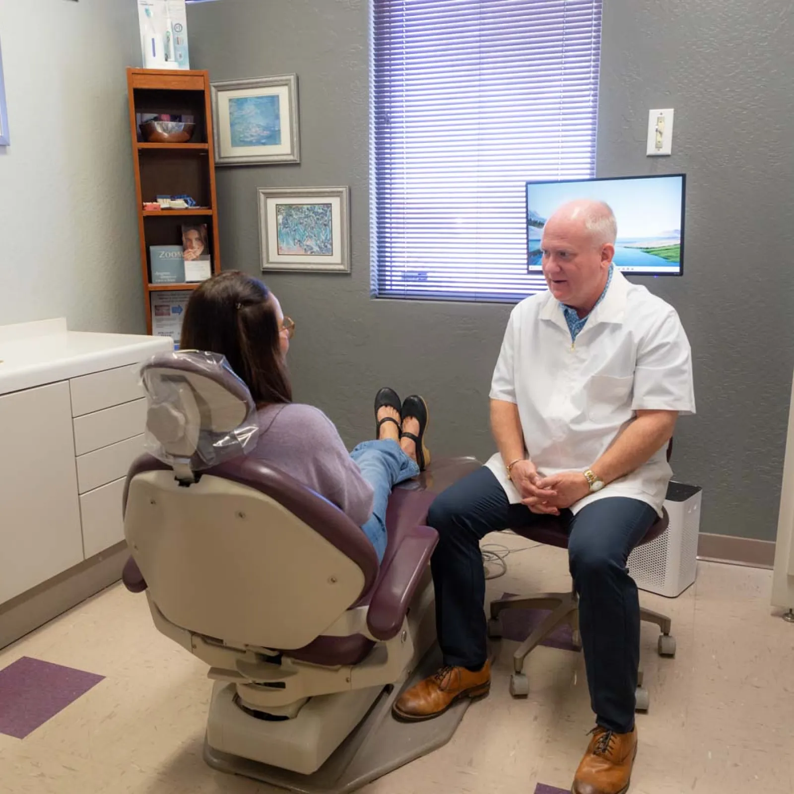 Dentist in white coat consulting female patient seated in a dental chair in a modern clinic room