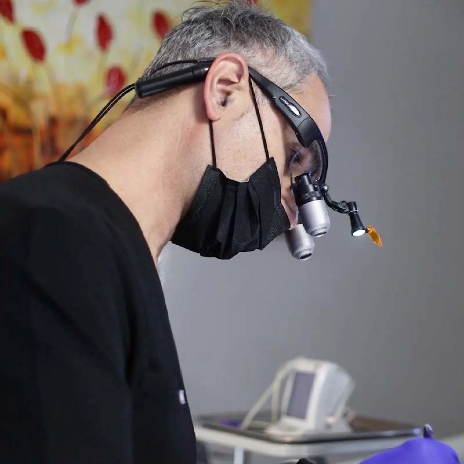 Close-up of a medical professional wearing magnifying loupes and a black mask performing a precise procedure.