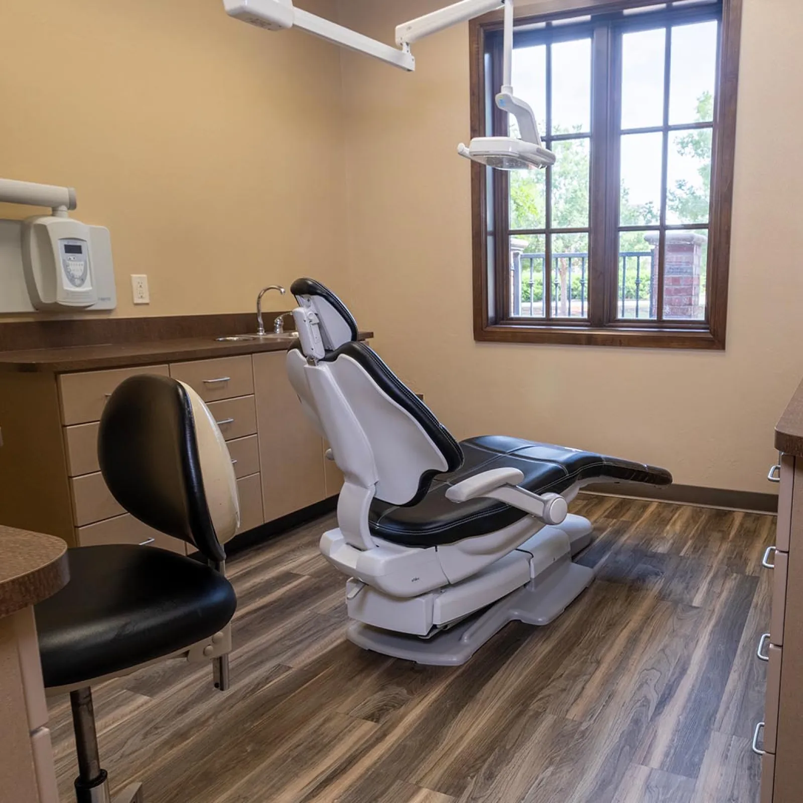 Modern dental clinic room with adjustable patient chair, wooden flooring, and natural light from window.