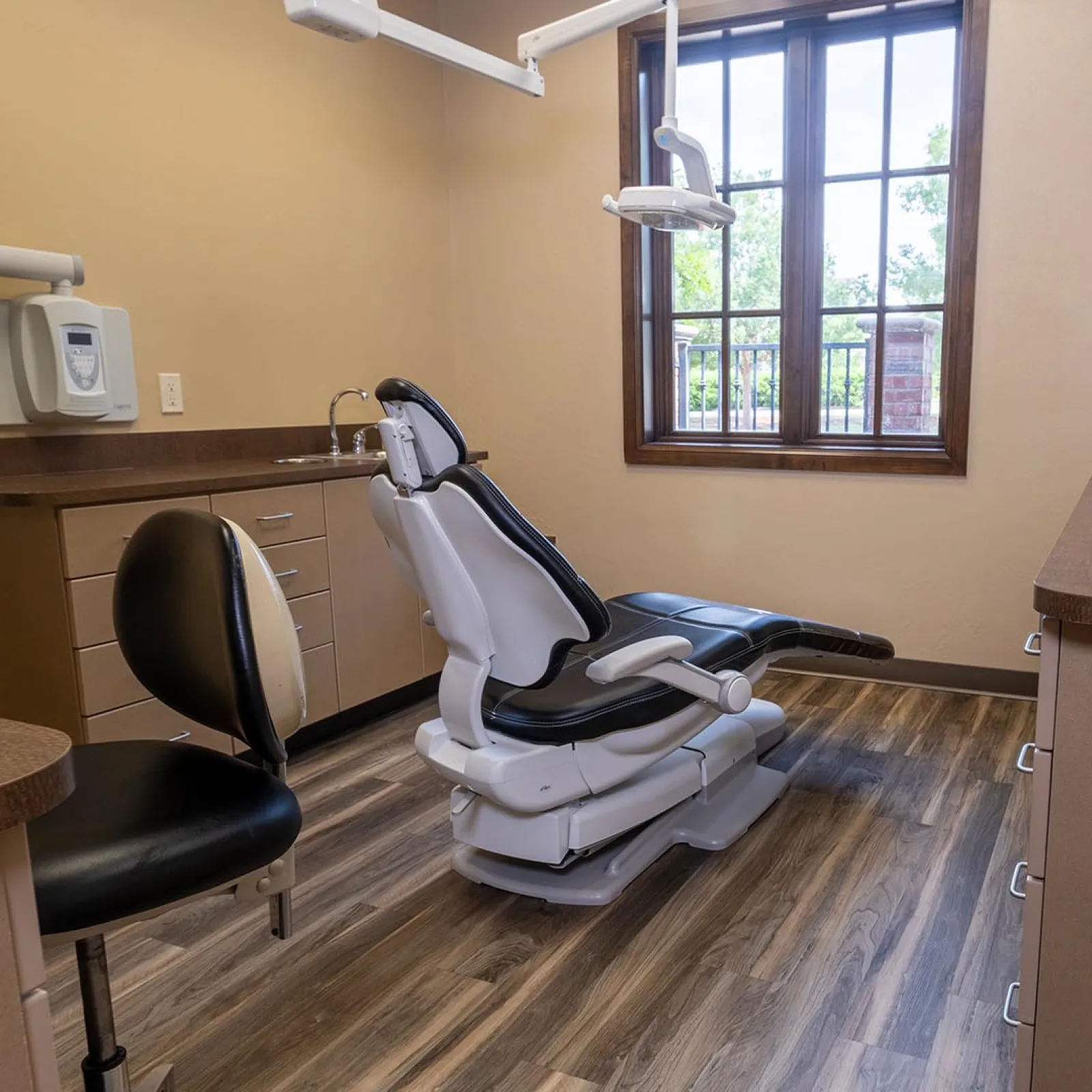Modern dental clinic room with adjustable patient chair, wooden flooring, and natural light from window.