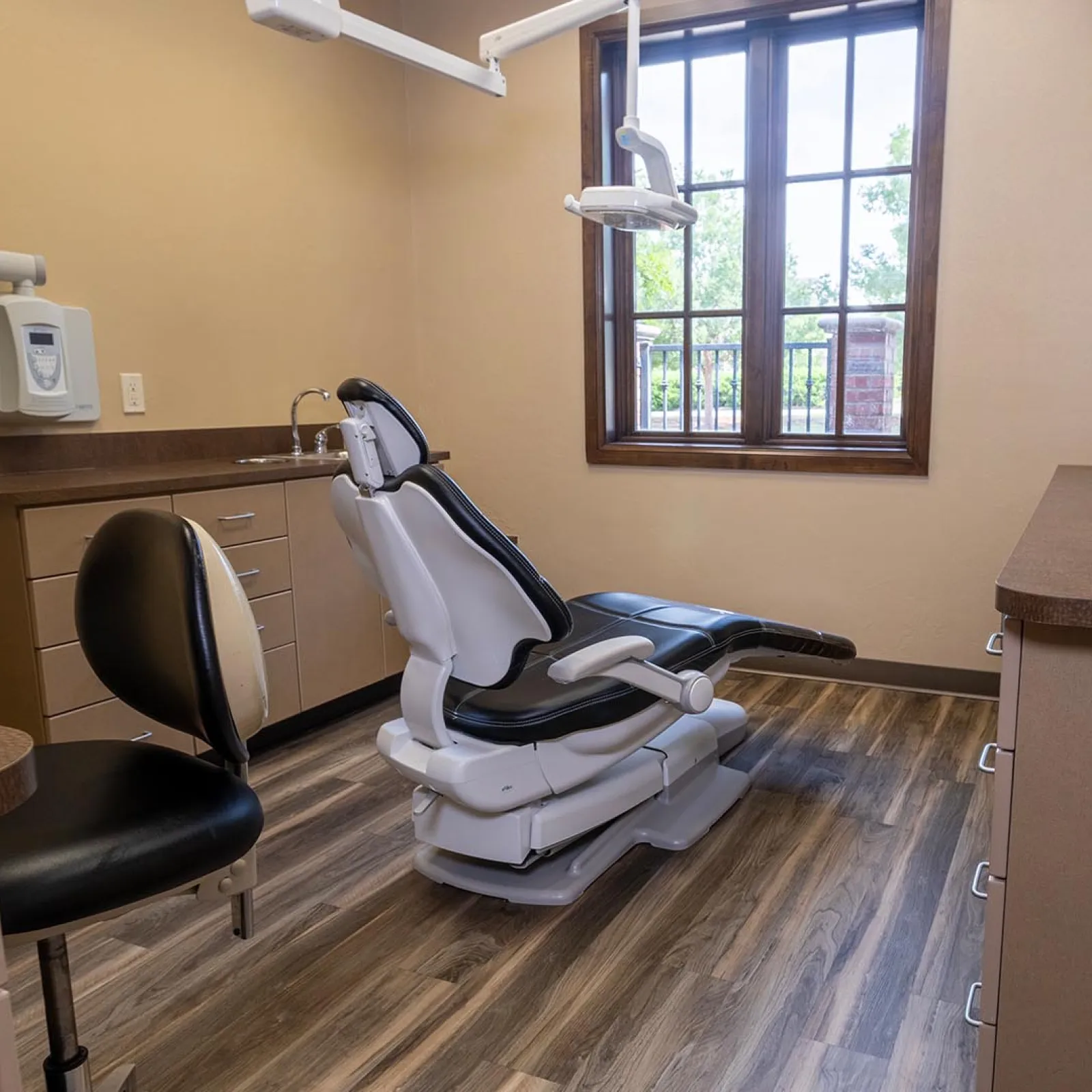 Modern dental clinic room with adjustable patient chair, wooden flooring, and natural light from window.