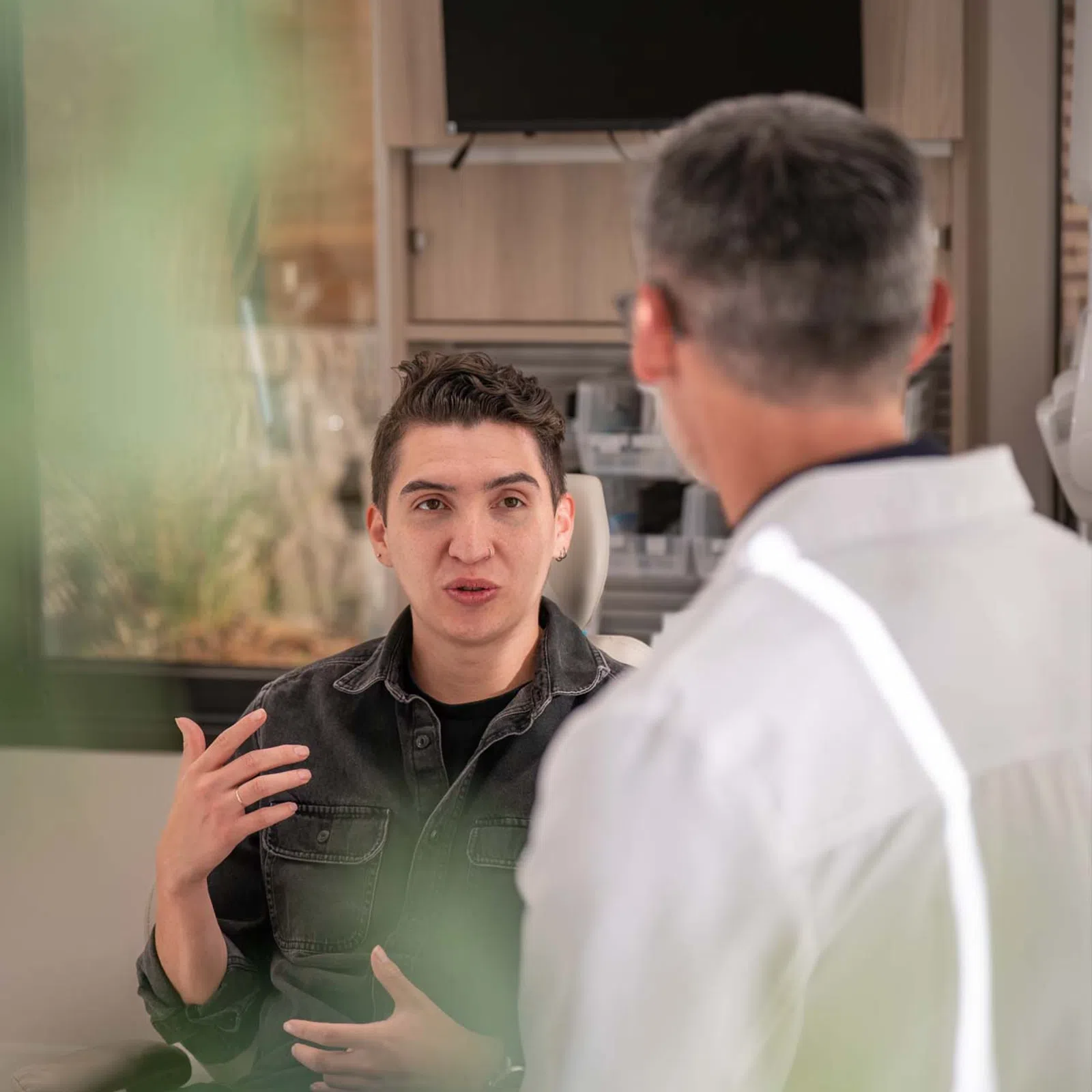 Young man explaining symptoms to doctor in medical office during consultation appointment.