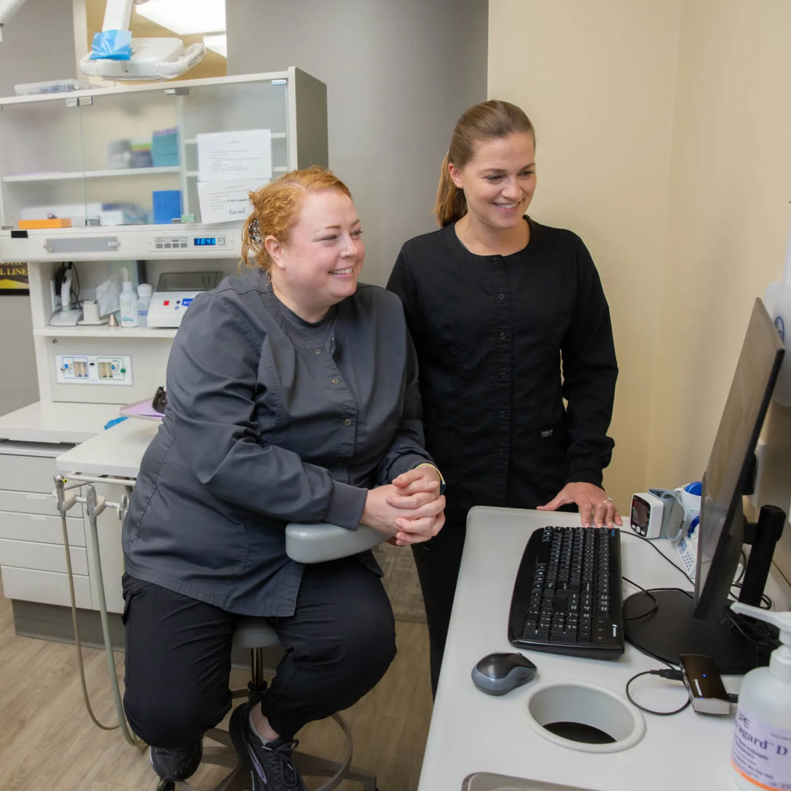 Two dental professionals review patient information on a computer in a modern dental office setting.