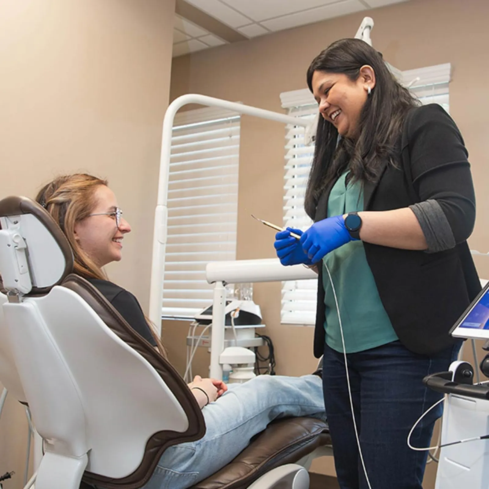 Dentist speaking with smiling patient in dental chair during a dental checkup in a clinic room.