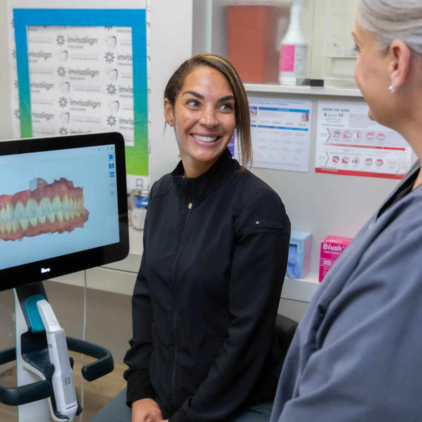 Dentist and patient smiling during a dental consultation with 3D teeth scan on computer screen.