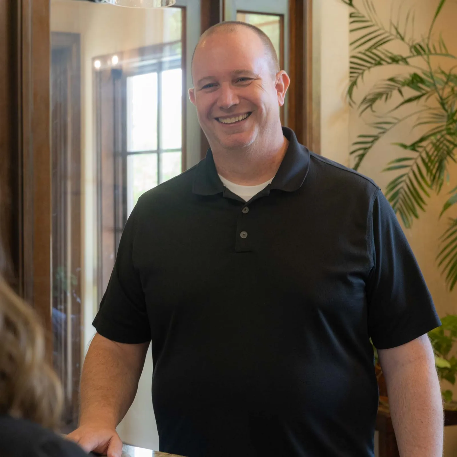 Smiling man in black polo shirt talking to woman with long hair in cozy home interior.