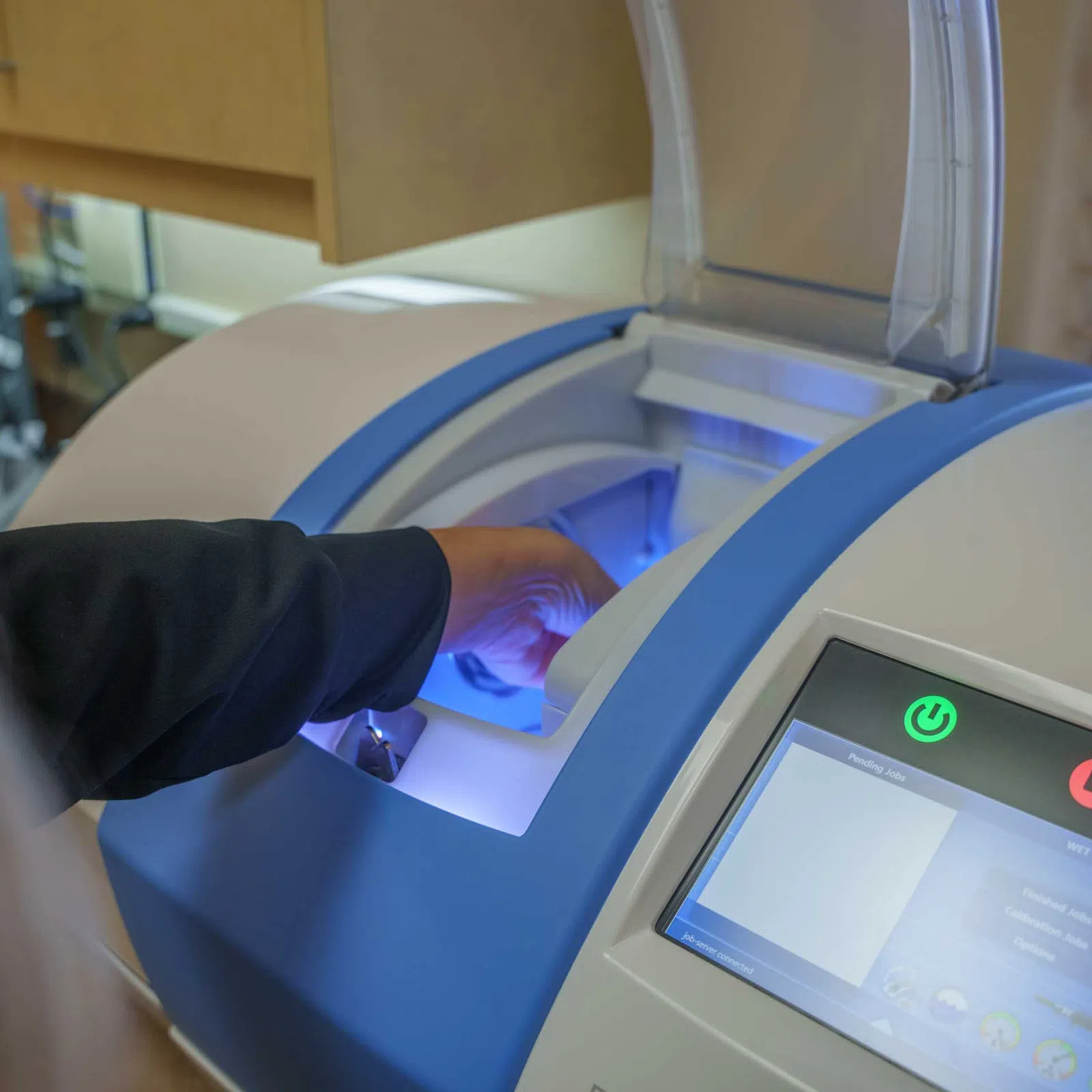 Person operating a dental 3D scanner machine with blue light for precise modeling.