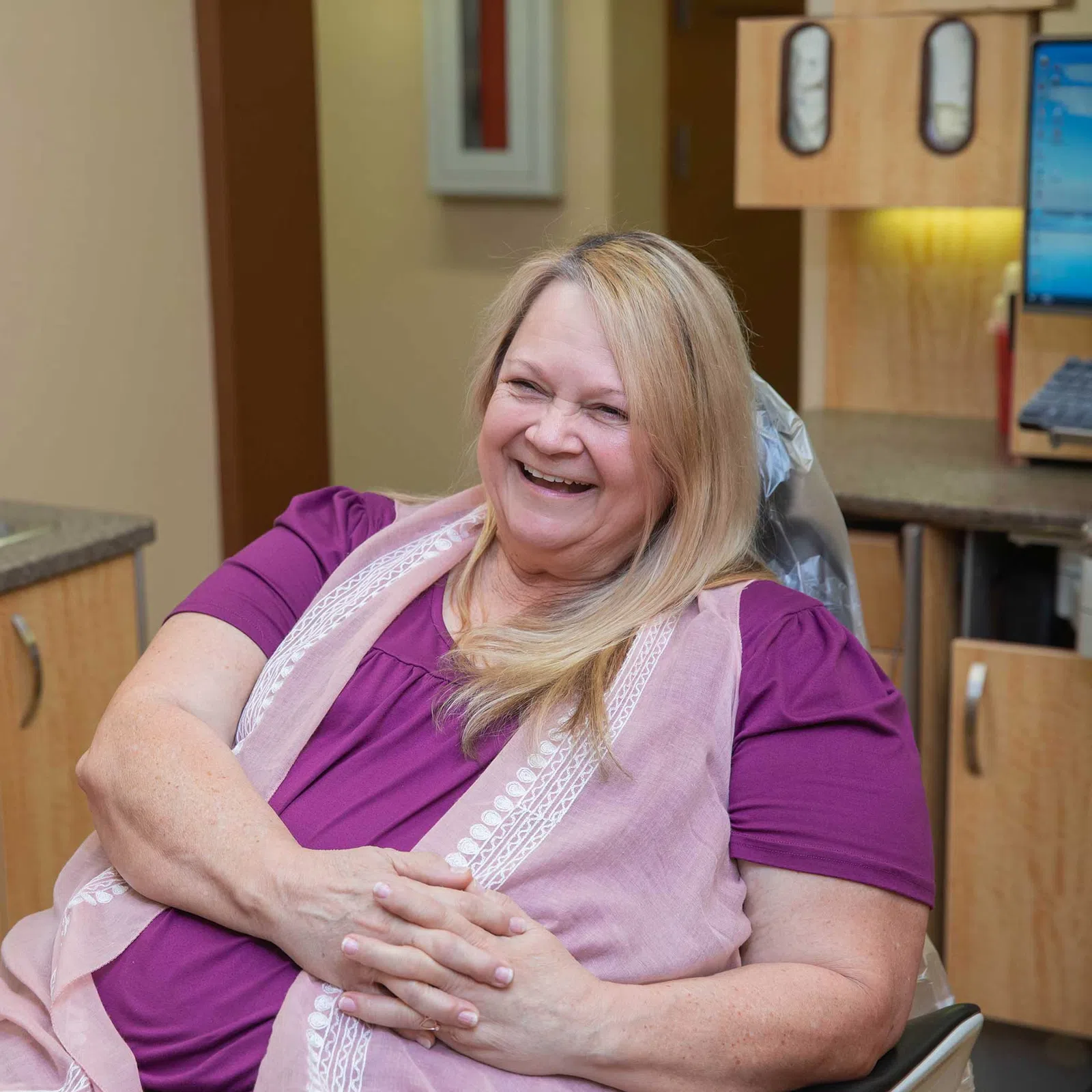 Smiling middle-aged woman in casual clothes sitting and relaxing in a dental office chair.