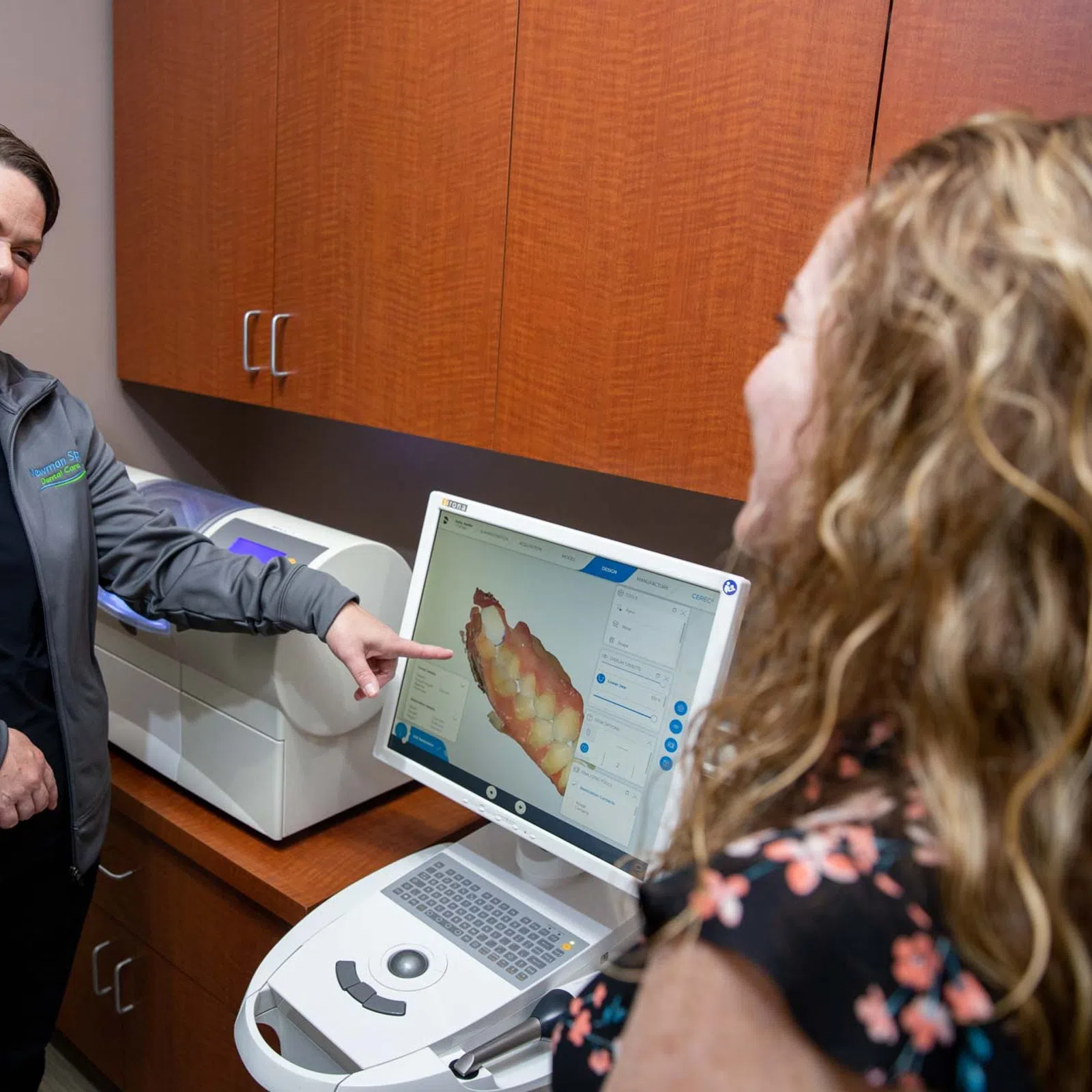 Dental professional showing a 3D teeth scan on a computer to a smiling patient in a clinic.