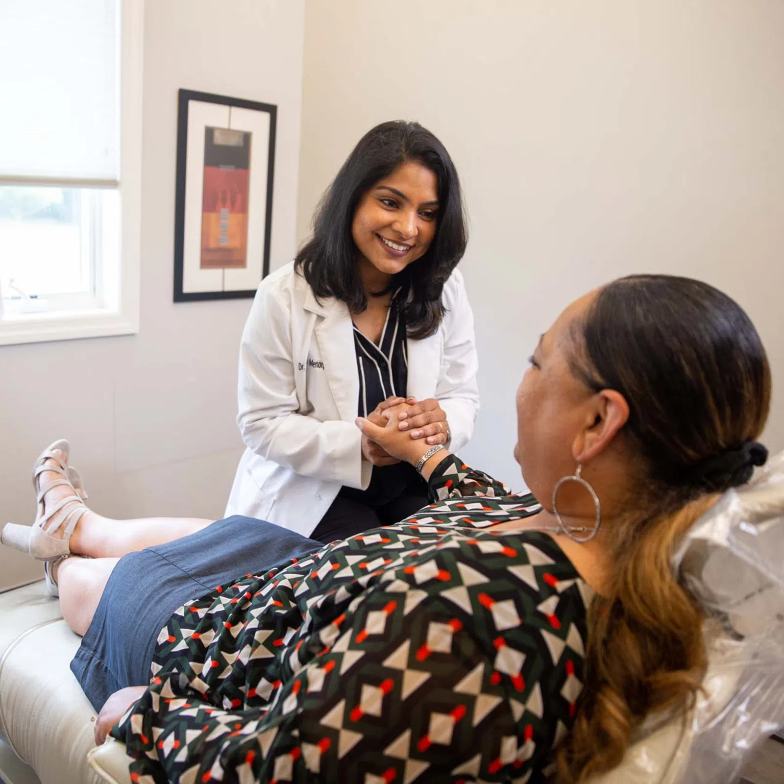 Female doctor smiling and holding hands with patient lying on medical exam table in bright office