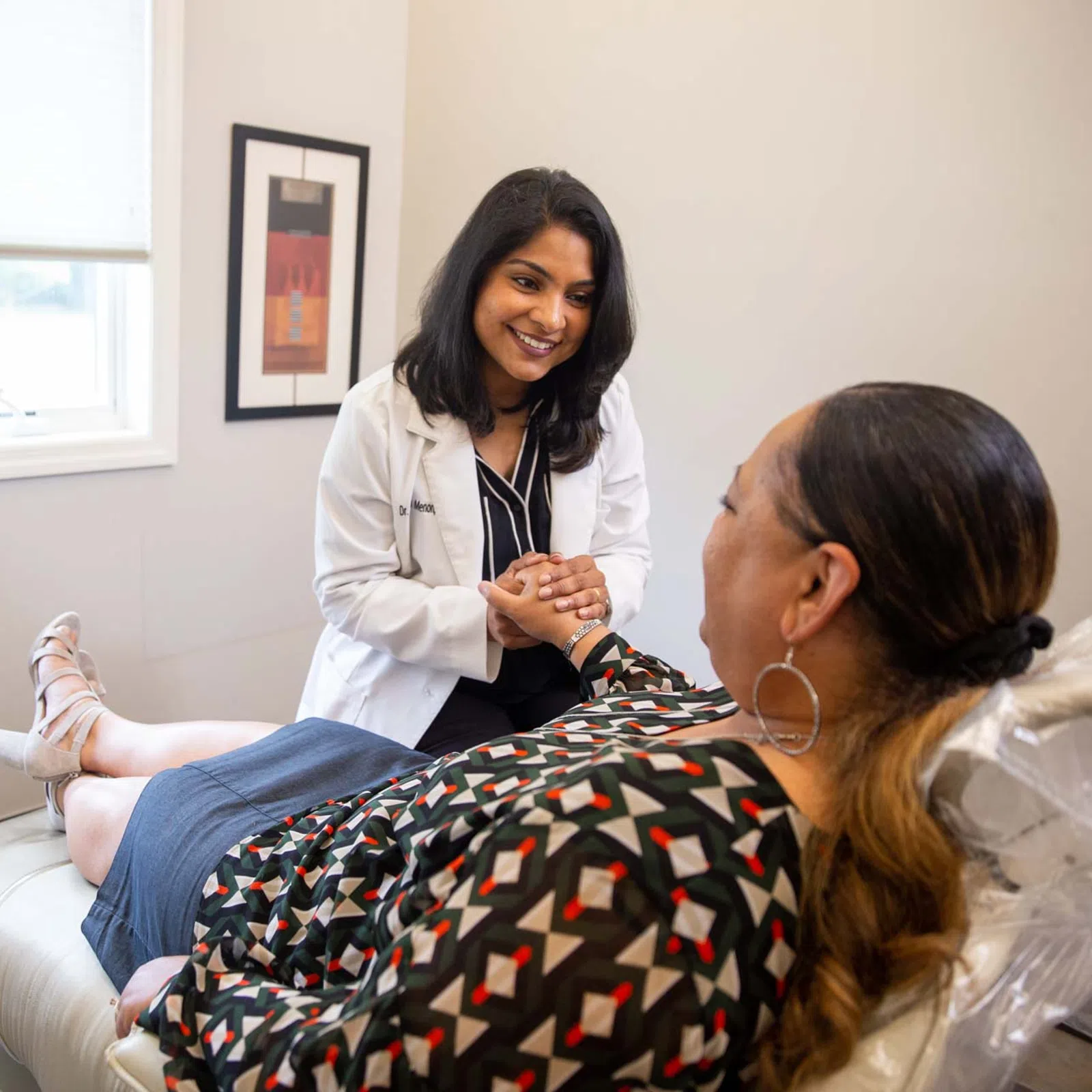 Female doctor smiling and holding hands with patient lying on medical exam table in bright office