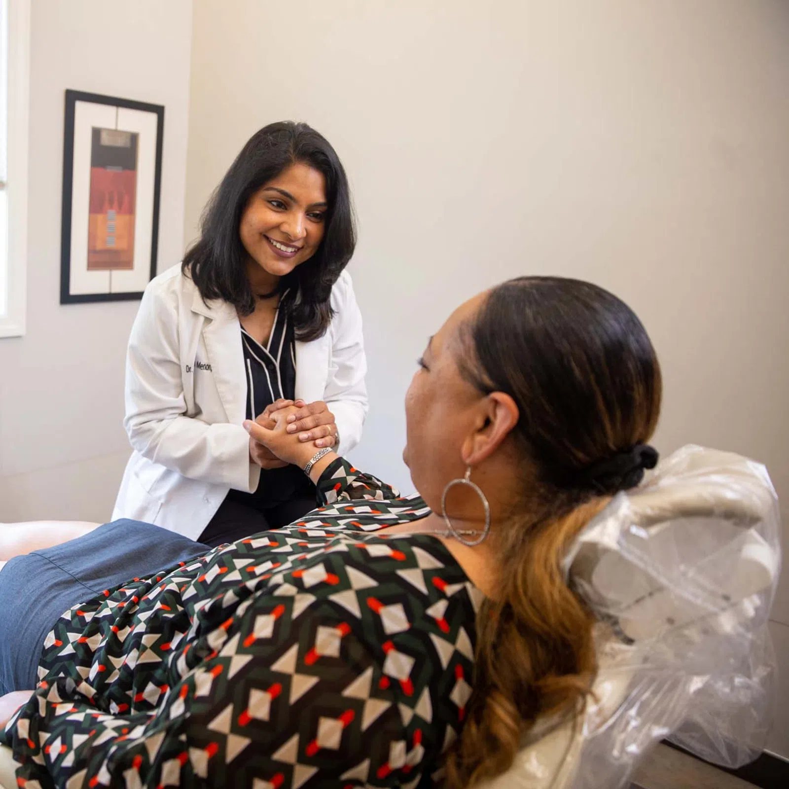 Female doctor smiling and holding hands with patient lying on medical exam table in bright office