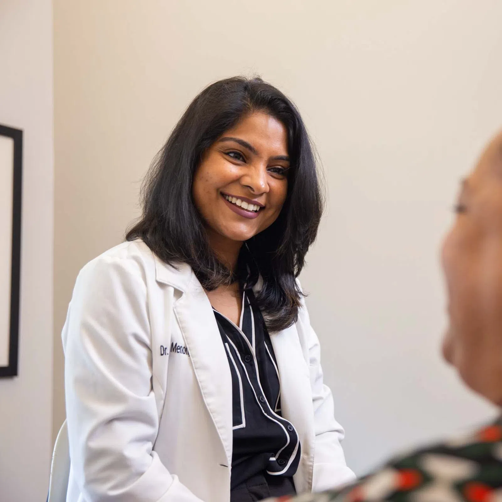 Female doctor in white coat smiling and talking with a patient during a consultation in a medical office.
