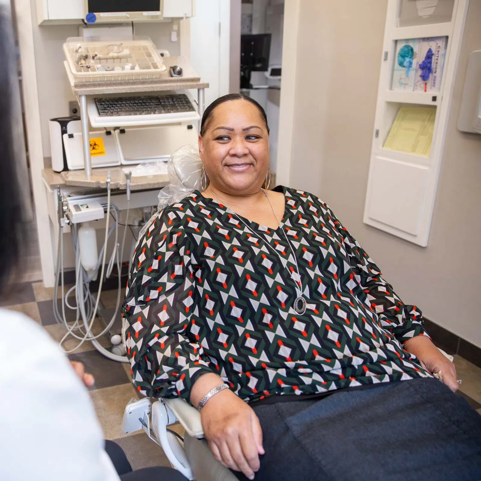 Smiling woman sitting in dental chair talking to a dentist in a modern clinic room.