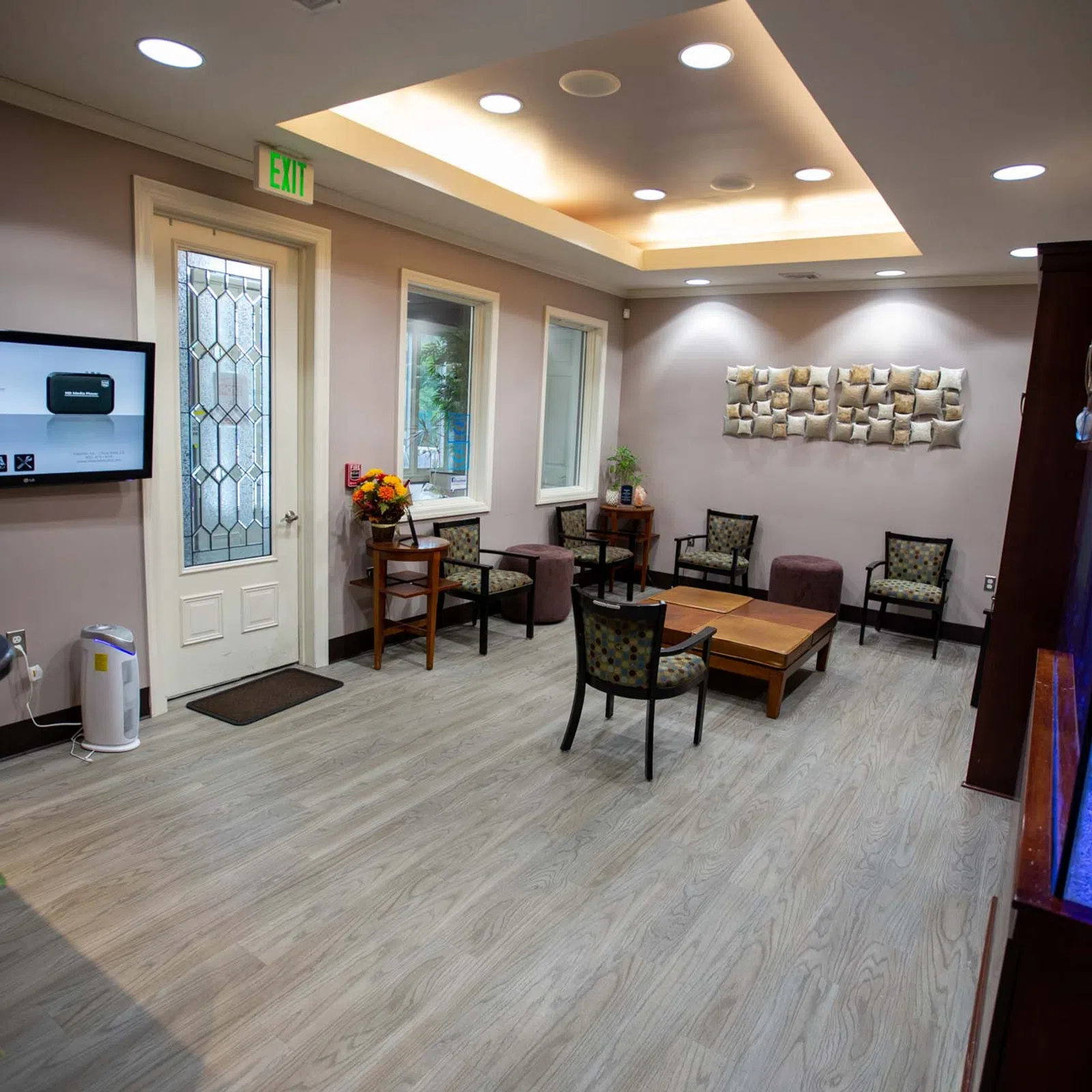 Modern waiting room with chairs, wooden table, wall art, aquarium, and television screen near entrance door.