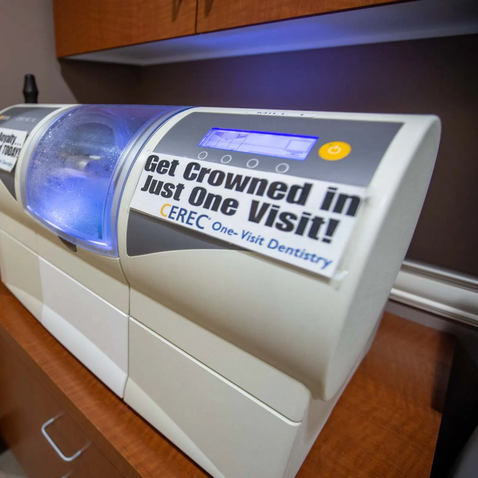 CEREC dental machine in office with sign promoting same-day crown services in one visit.
