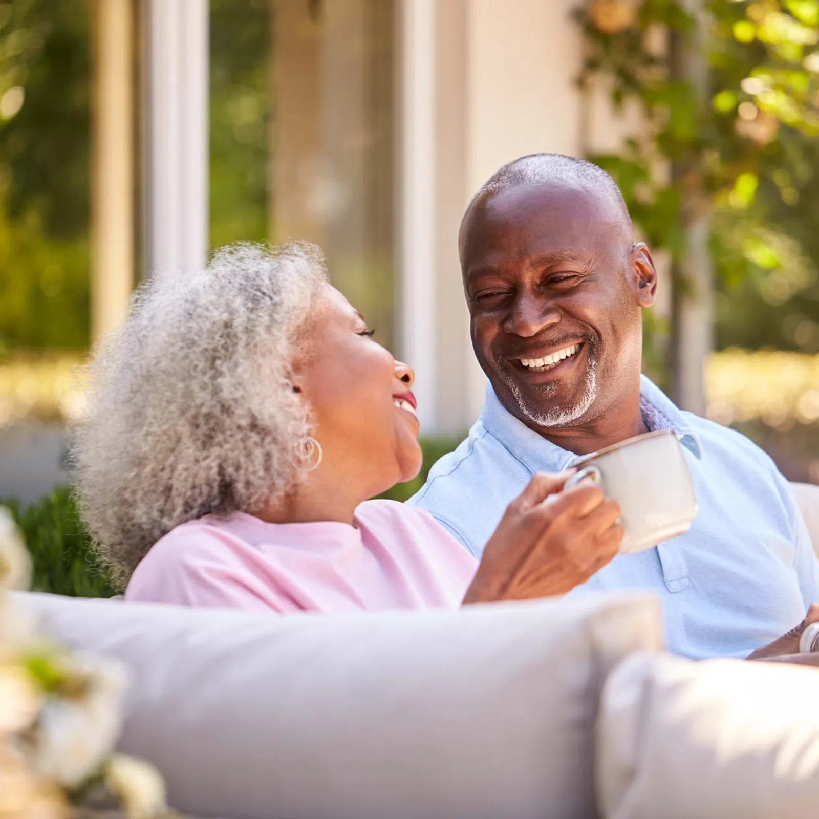 Happy senior couple smiling and enjoying coffee together outdoors on a sunny day.