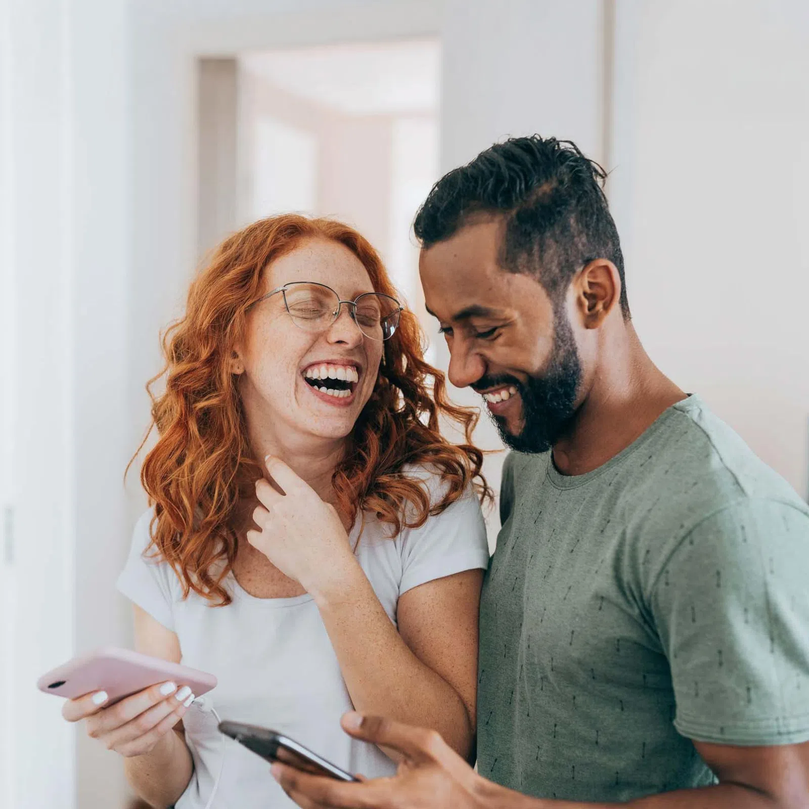 Couple laughing together while holding smartphones in a cozy modern living room setting