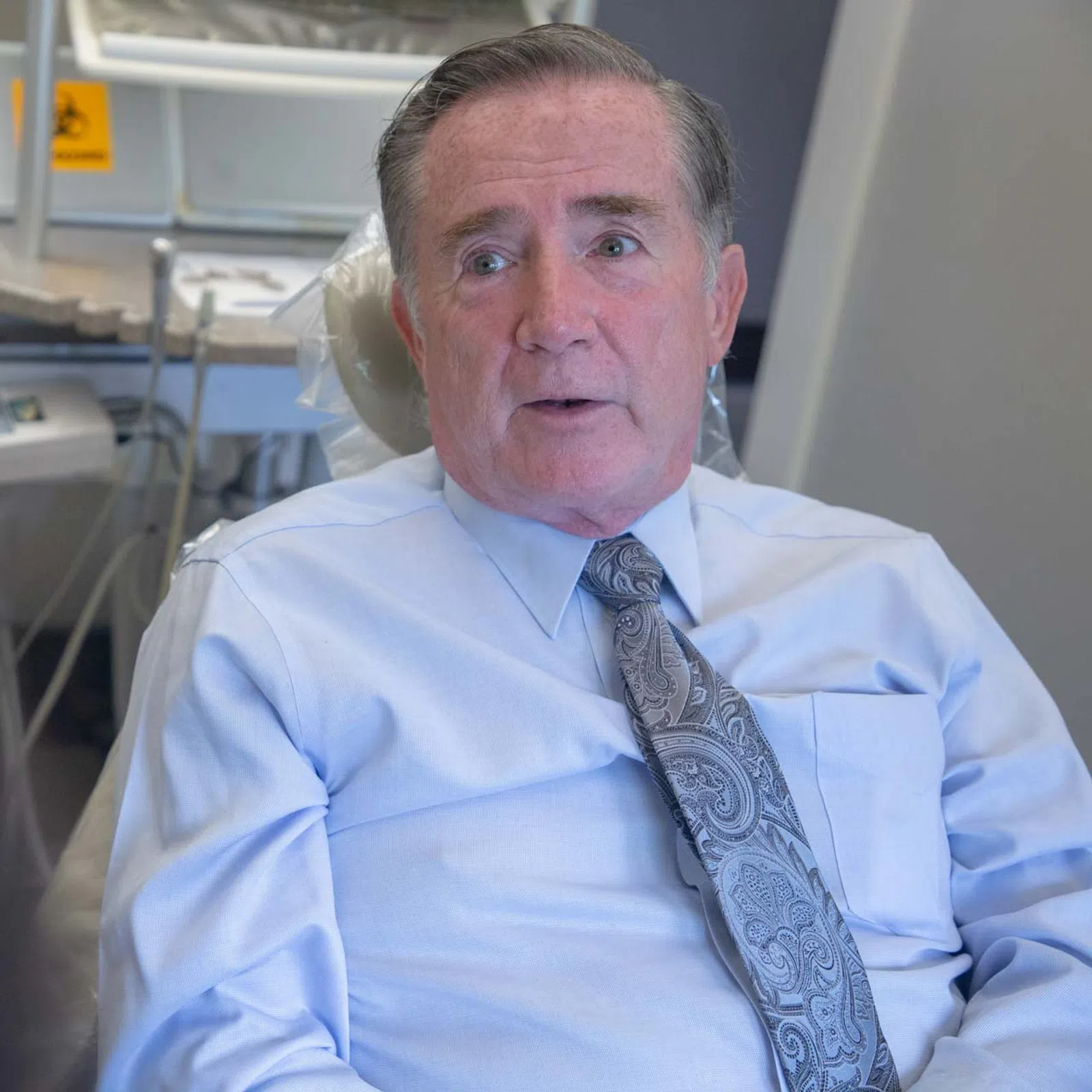 Middle-aged man in business attire sitting in a dental chair with dental equipment in the background