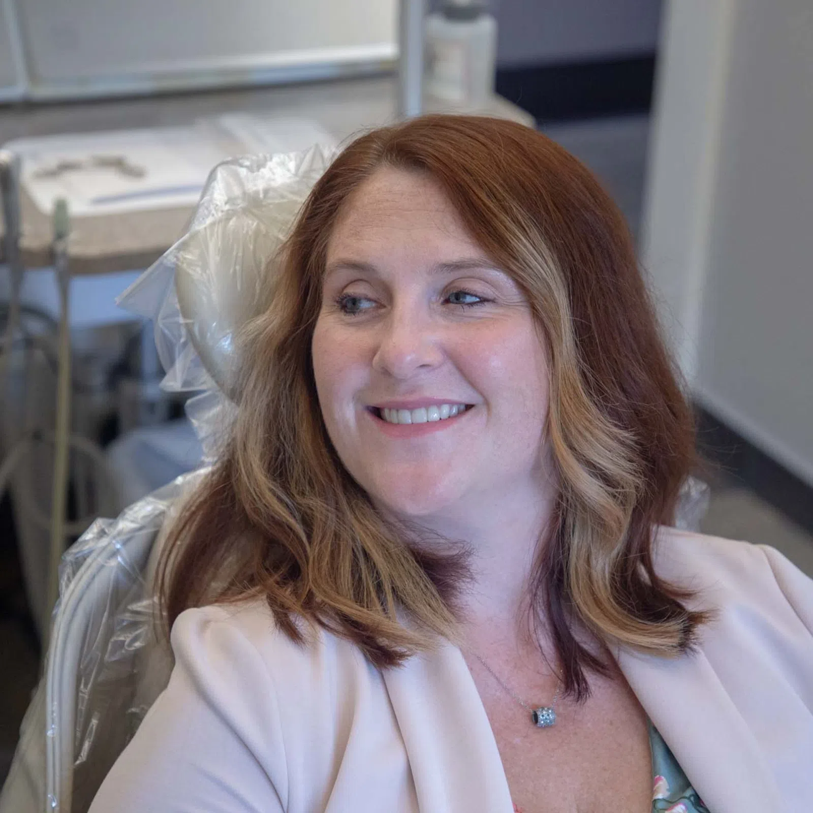 Smiling woman with shoulder-length hair sitting in a dental chair in a modern dental office.