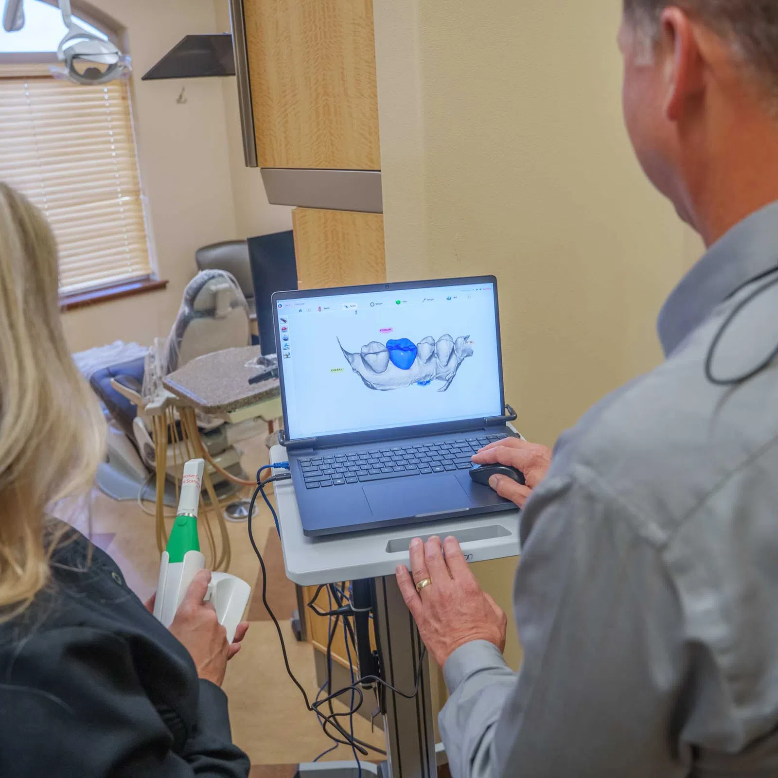 Dentist and assistant review a 3D dental scan of teeth on a laptop in a dental office setting.