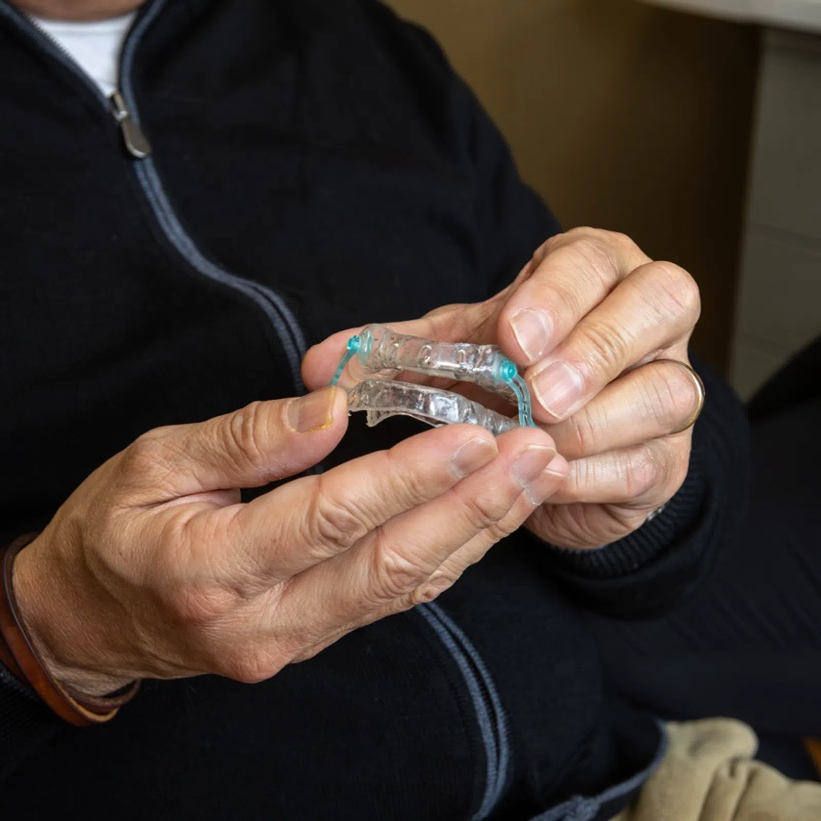 Close-up of a person holding a clear dental retainer with hands in a casual setting.