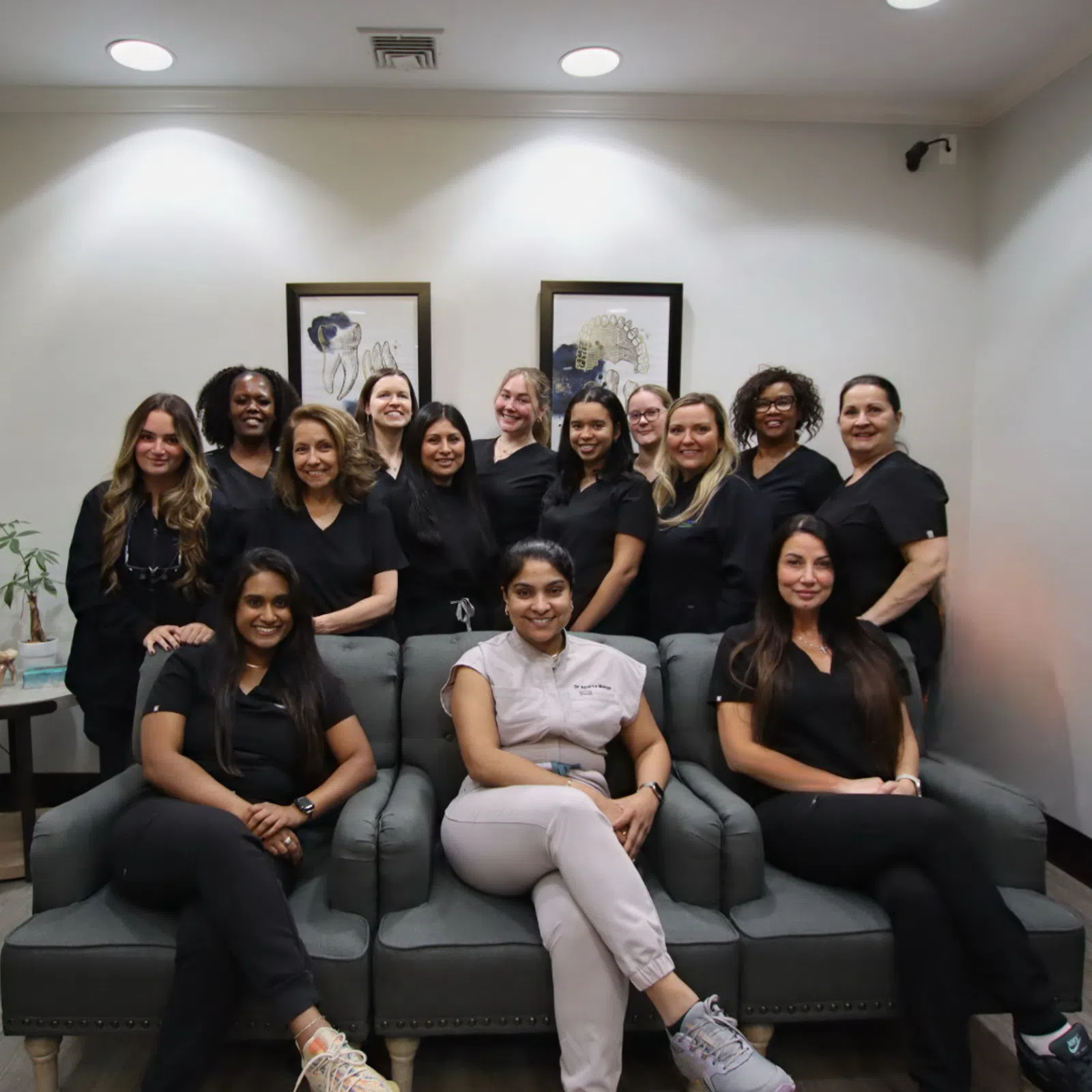 Group of smiling female professionals in black and white uniforms posing in a modern office lounge area.
