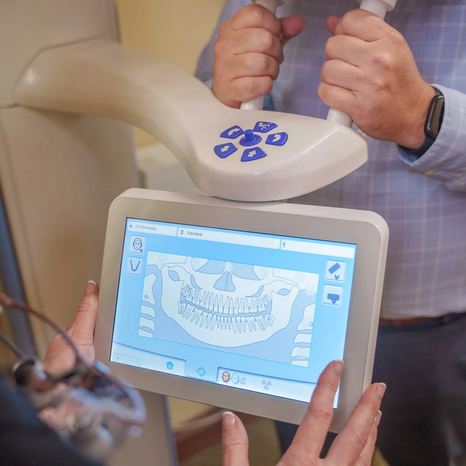 Dental professional using 3D X-ray machine showing jaw and teeth on touchscreen monitor in clinic.