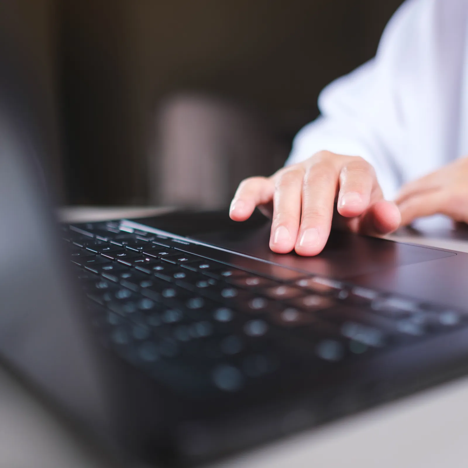 Close-up of a person using a laptop with fingers on the keyboard in a softly lit environment.
