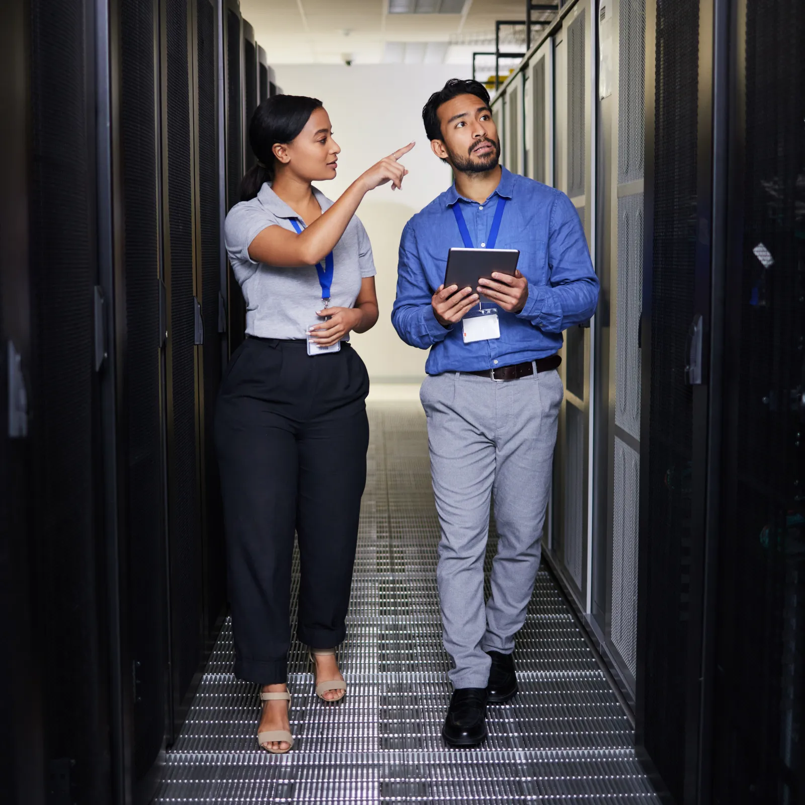 Two IT professionals discussing while walking through a data center server aisle with a tablet