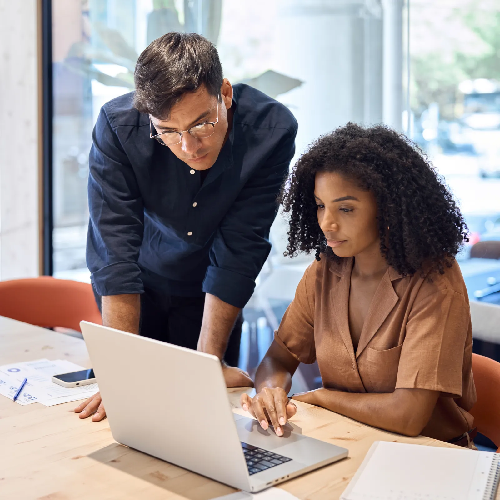 Three coworkers focused and collaborating while looking at a desktop monitor in a modern office setting.