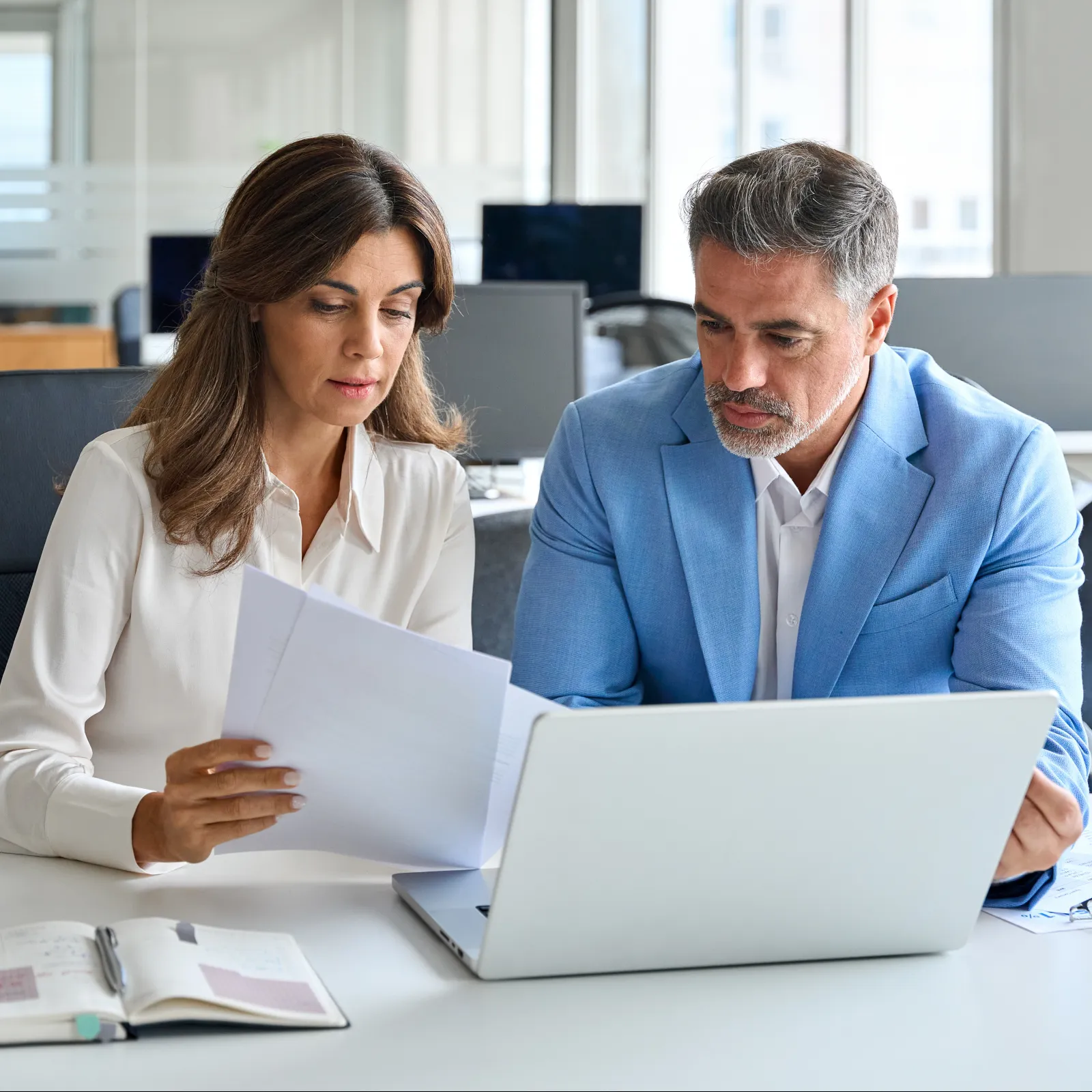 Three coworkers focused and collaborating while looking at a desktop monitor in a modern office setting.