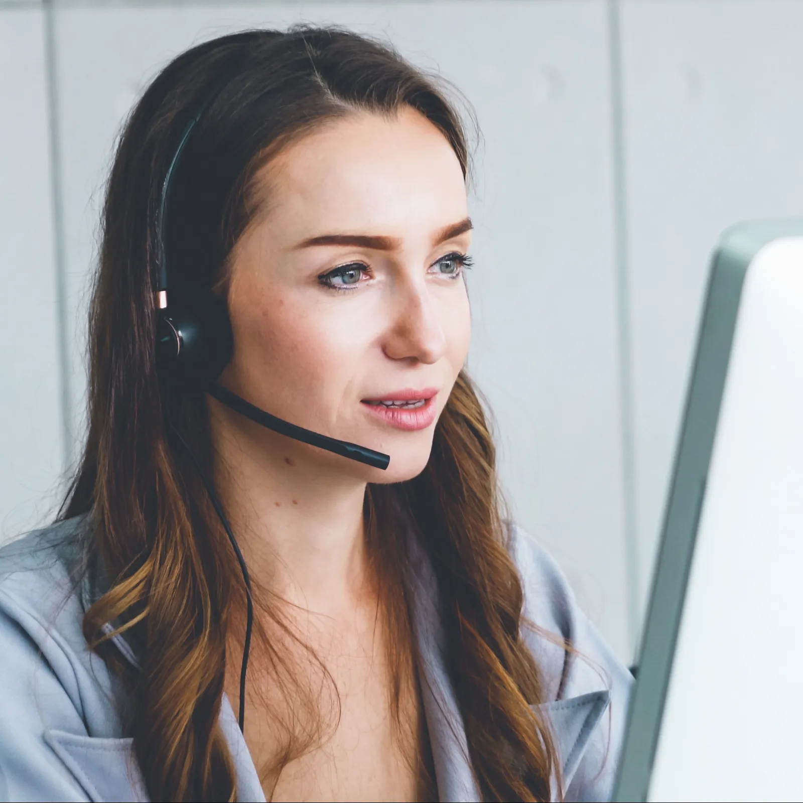 Young woman wearing headset working at computer providing customer support in modern office environment